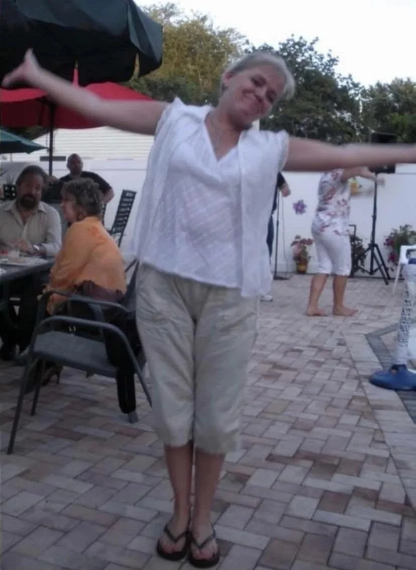 A woman dancing outdoors at a gathering or party with arms stretched out, smiling.