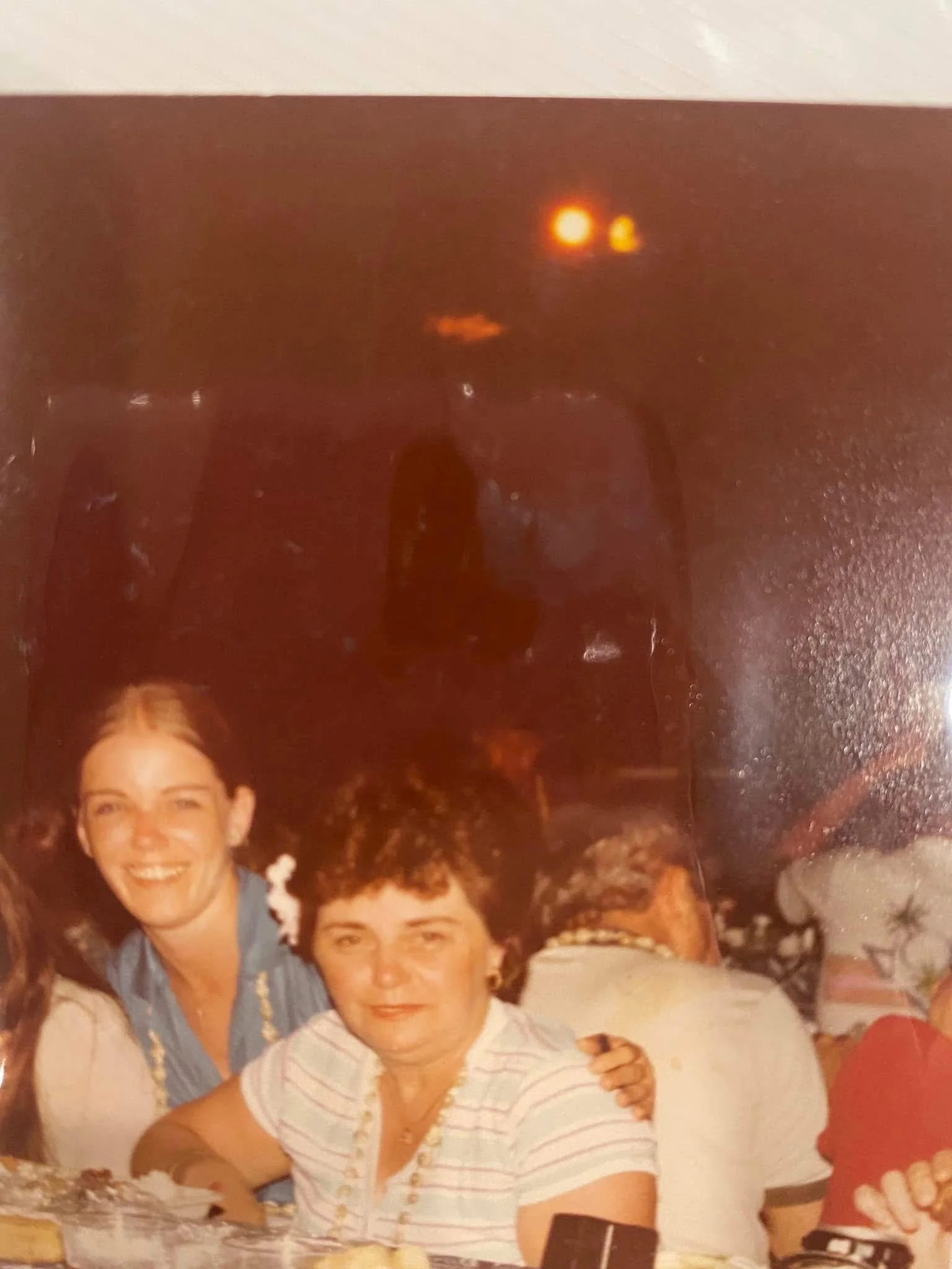 A photo of a smiling woman with short dark hair, wearing a white and gray striped shirt. There are other people around her, and the scene appears to be at a social gathering or party.