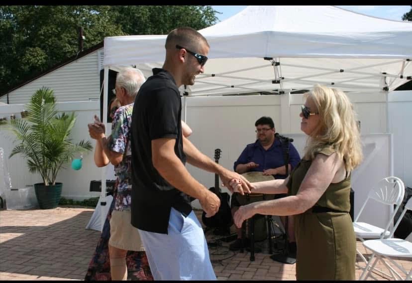 Two couples dancing outdoors at a social gathering with a band playing under a white tent.