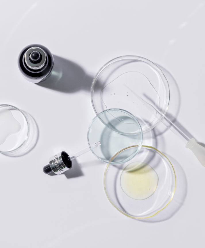 Laboratory scene with glass petri dishes, a dropper, and a small vial on a white surface.