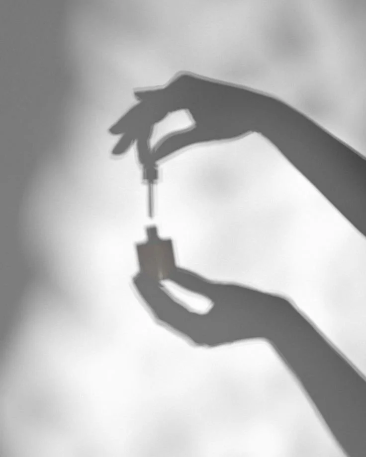 Silhouette of two hands handling a small vaccination vial and a syringe against a light background.