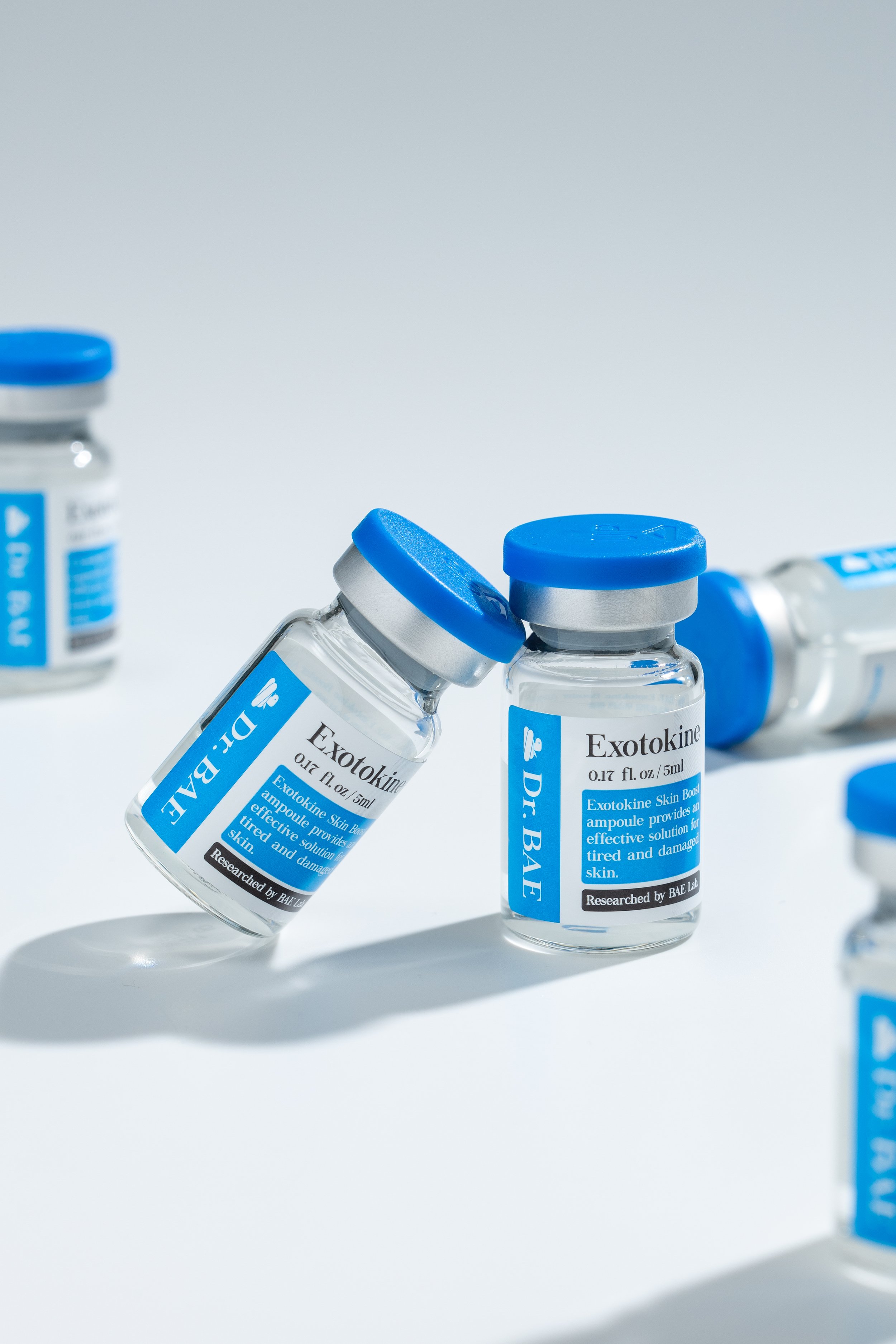 Several small medical vials labeled 'Exotokine' with blue caps, some are upright and others are tilted or lying down, on a white background.