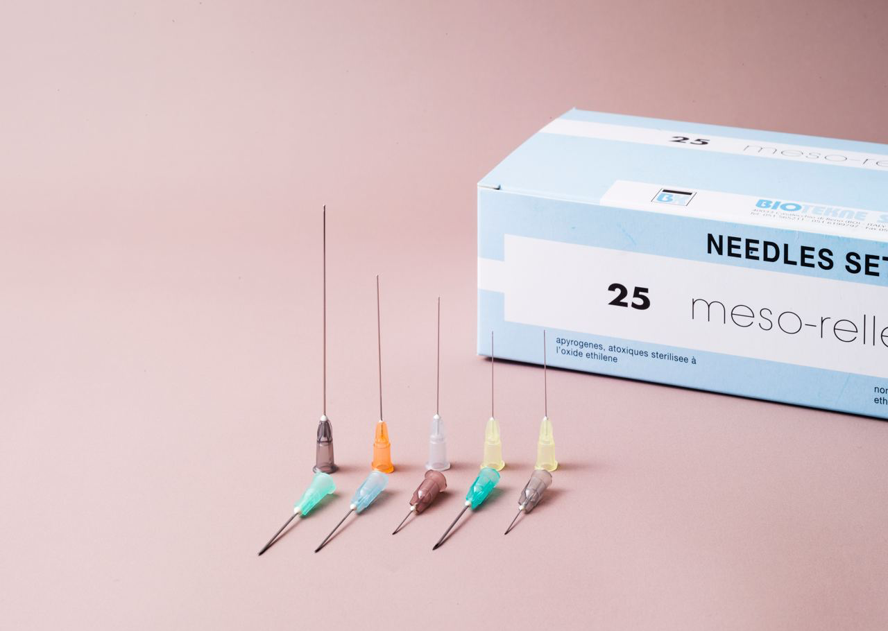 A box of 25 meso-roller needles next to five individual needles with different colored caps on a pink background.