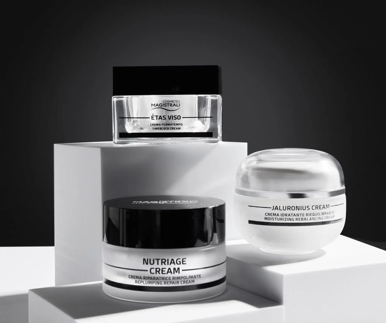 Three jars of skincare cream on white surfaces in a black and white photo.