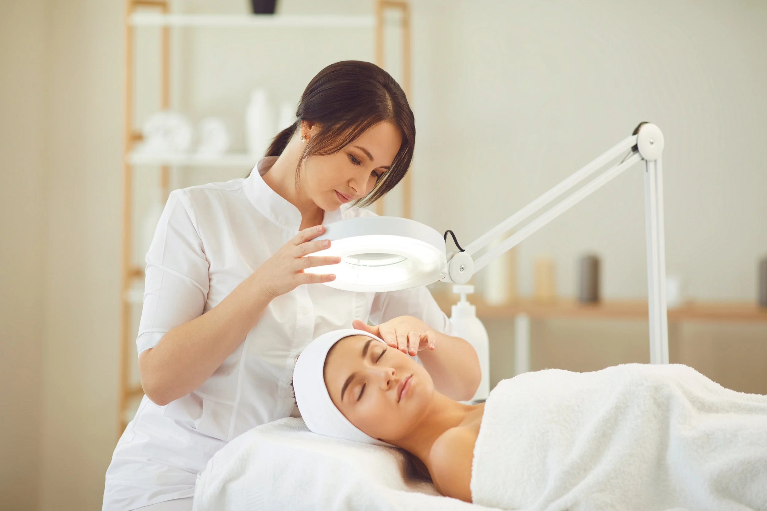 A woman receiving a facial treatment from a beautician in a spa or clinic setting.