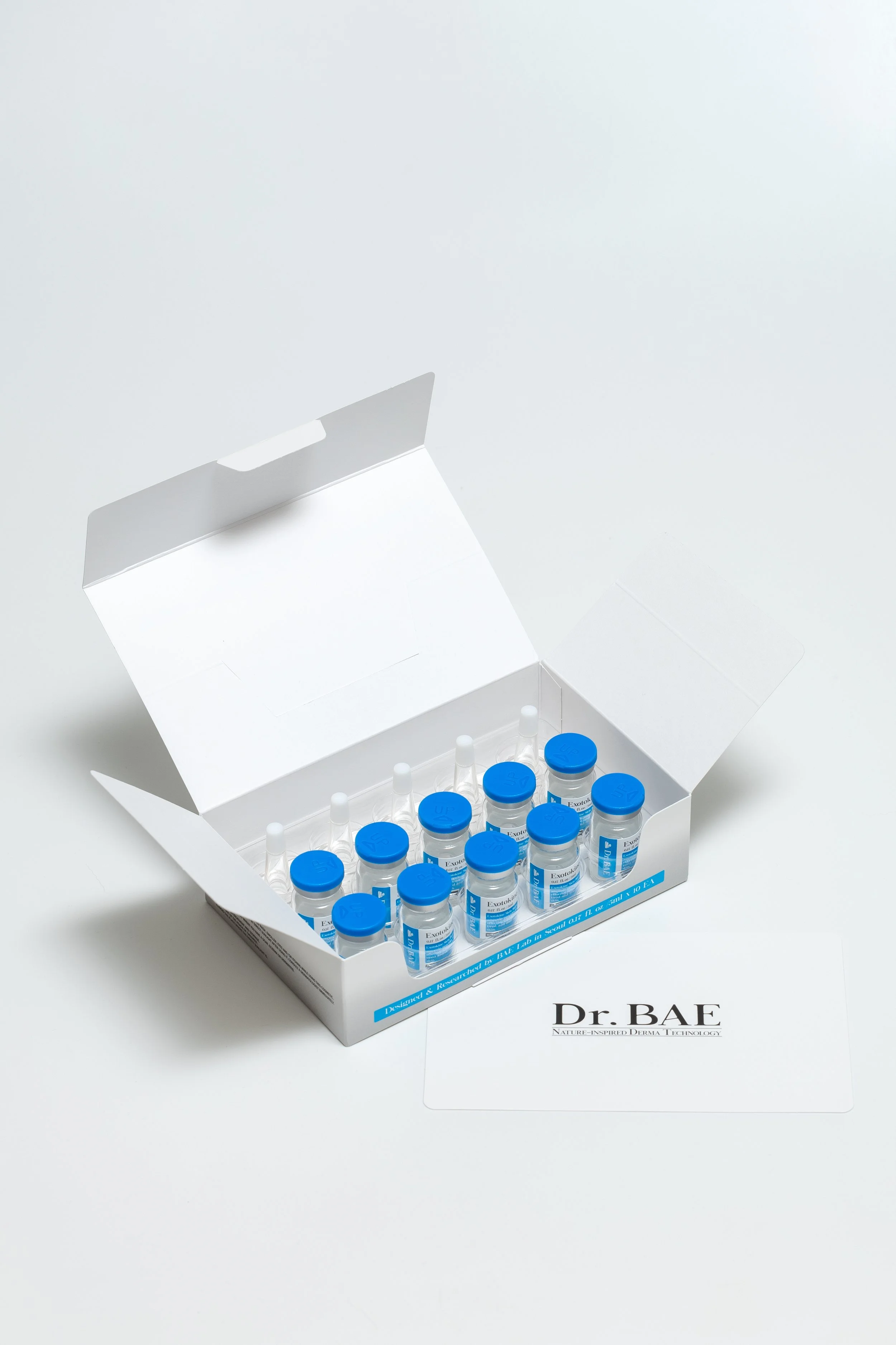Open white box labeled Dr. BAE containing multiple small vials with blue caps arranged in rows on a white surface.