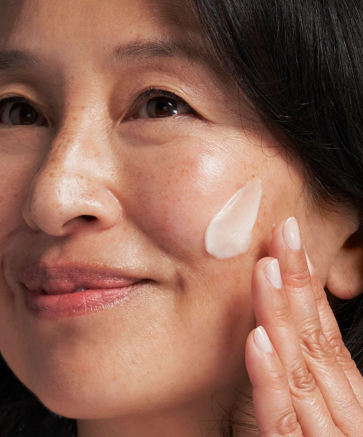 Close-up of a woman applying a cream or skincare product to her cheek with her finger.