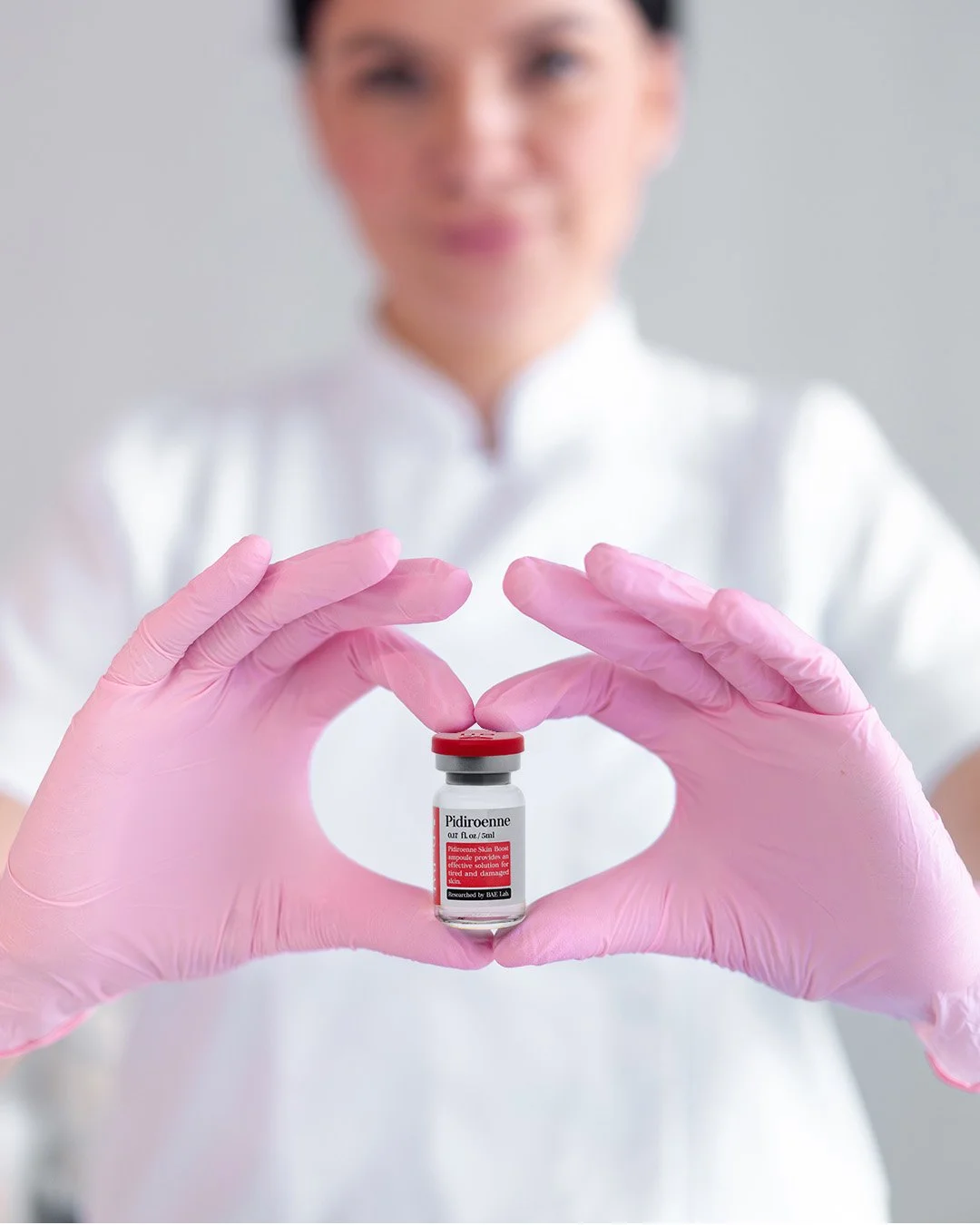 A healthcare professional wearing pink gloves holding a small vial labeled 'Pidiroenne' with a blurred background.