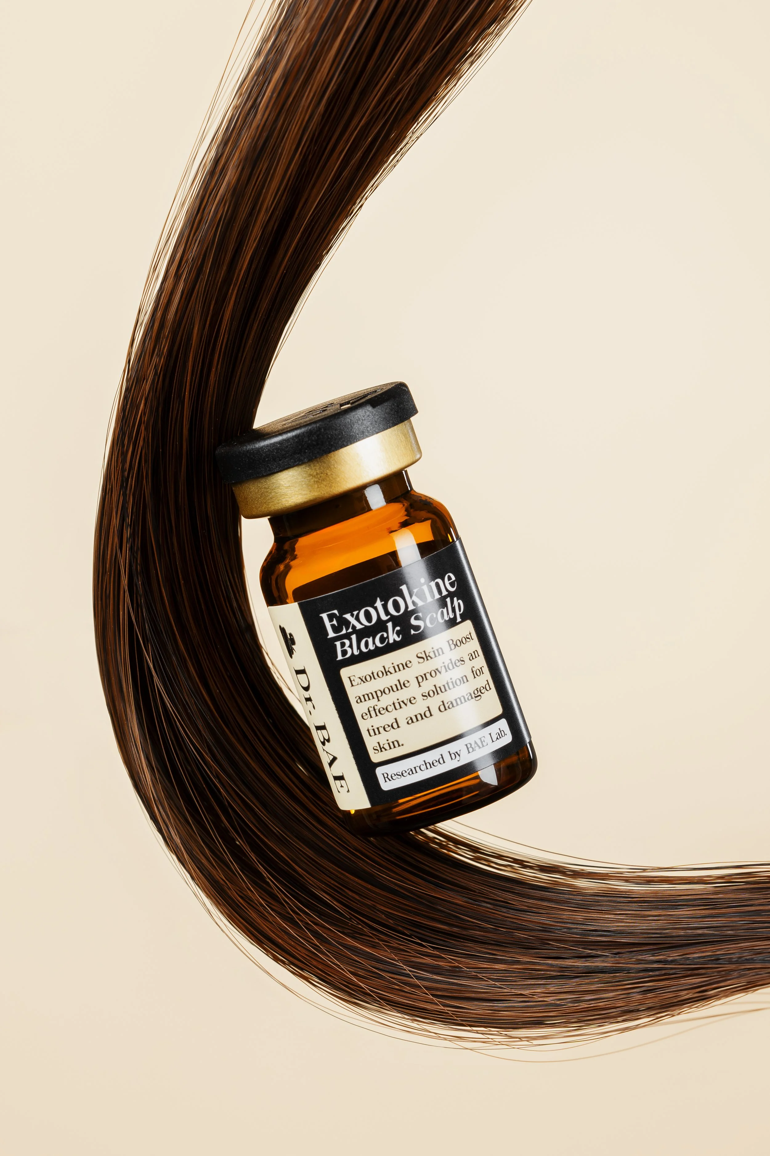 A small amber bottle labeled Exotokine Black Scalp, surrounded by a swirl of long, smooth, dark brown hair against a plain beige background.