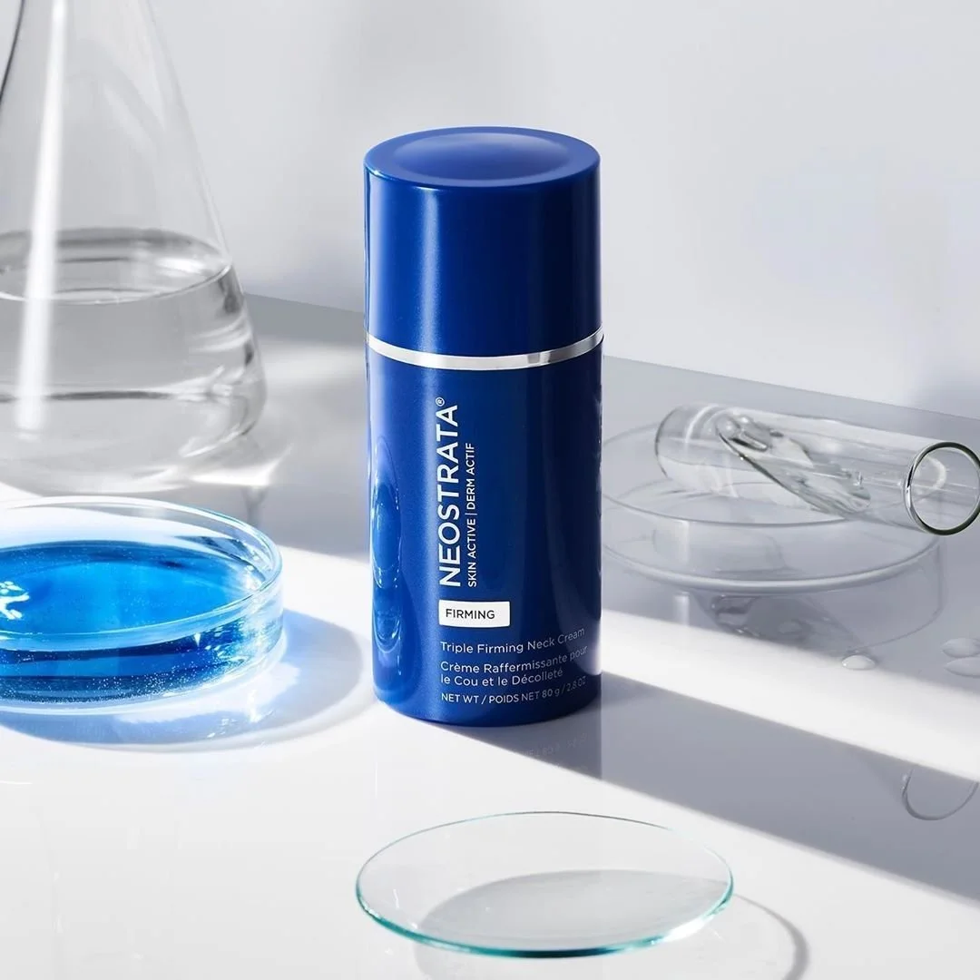 A blue canister of Neostrata Triple Firming Neck Cream on a white surface with glass labware around it.