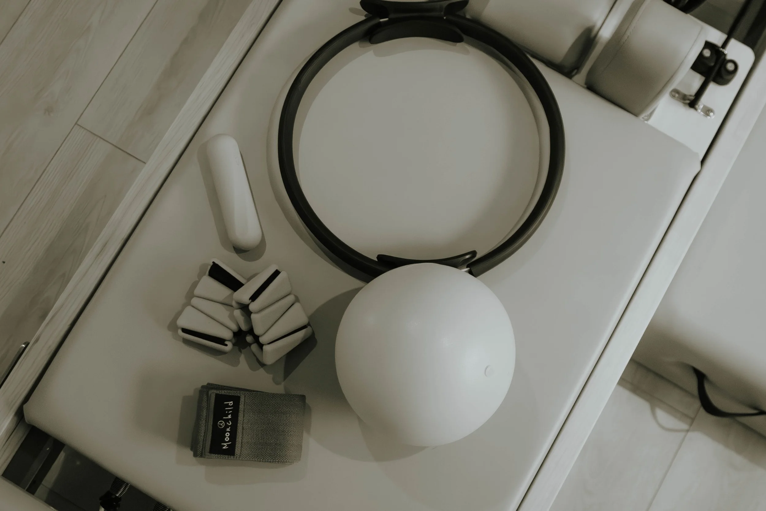 A top-down view of a white toilet with a black toilet seat, a pile of white and black sanitary pads, a black and grey wallet, and a small black device on a white countertop against a wall with light-colored wooden flooring.