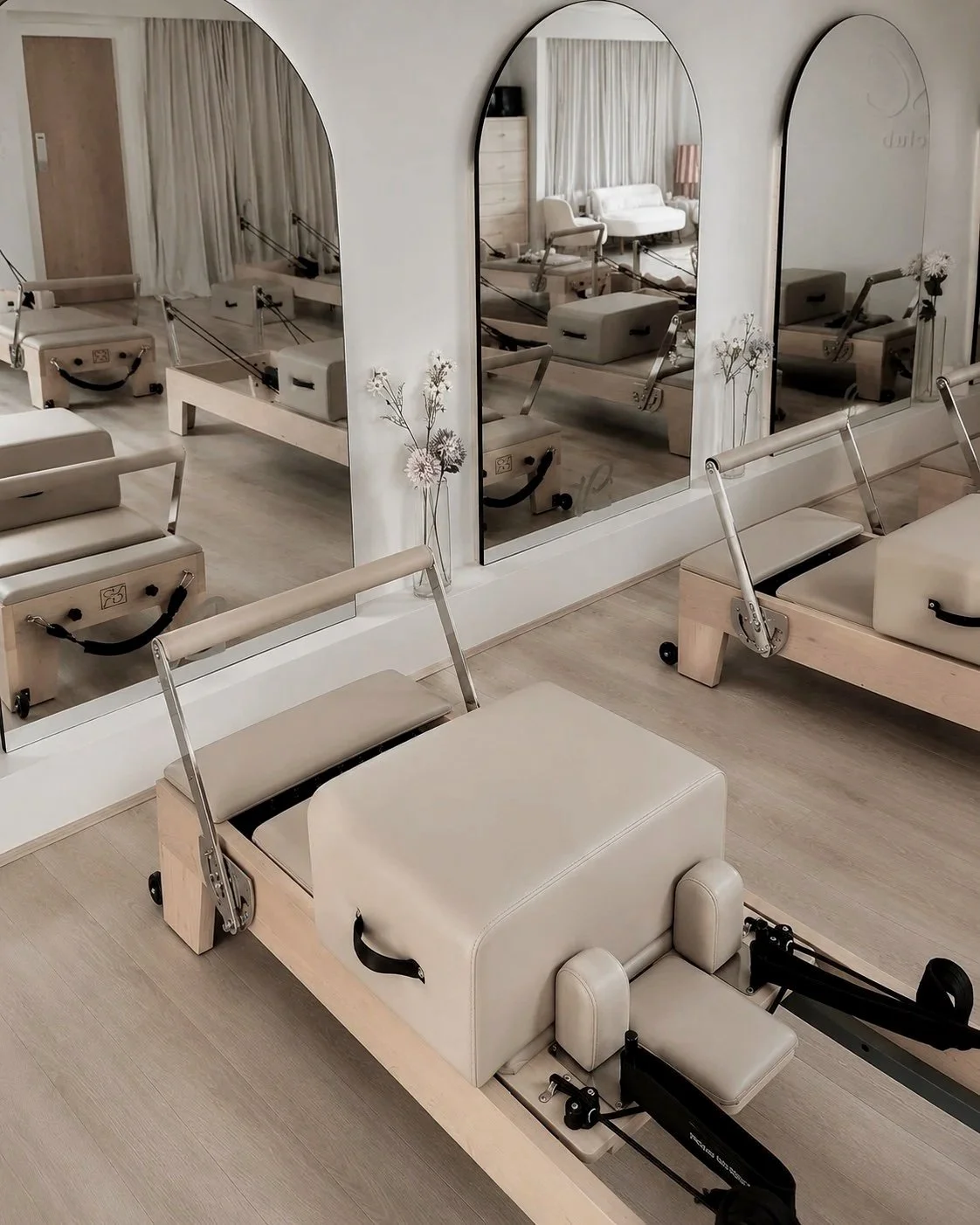 A fitness or physical therapy studio with Pilates reformer machines, large mirrors on the wall, and minimalist decor.