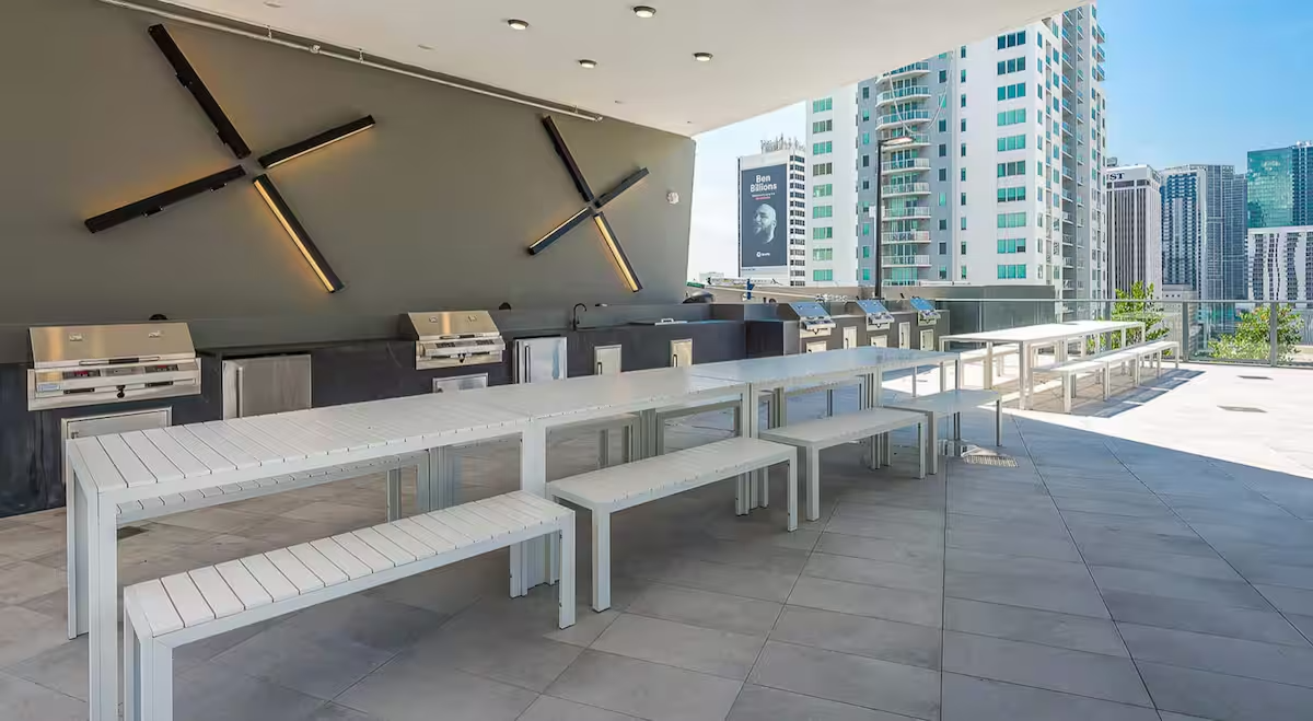 An outdoor balcony with white benches, modern steel grills, and a city skyline in the background.