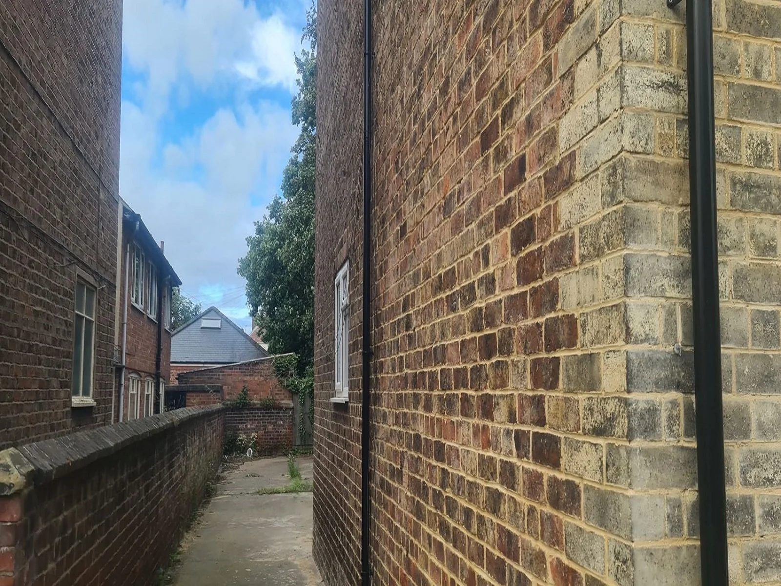 Side elevation of a brick property showing freshly completed lime mortar re-pointing on old brickwork next to a concrete pathway.