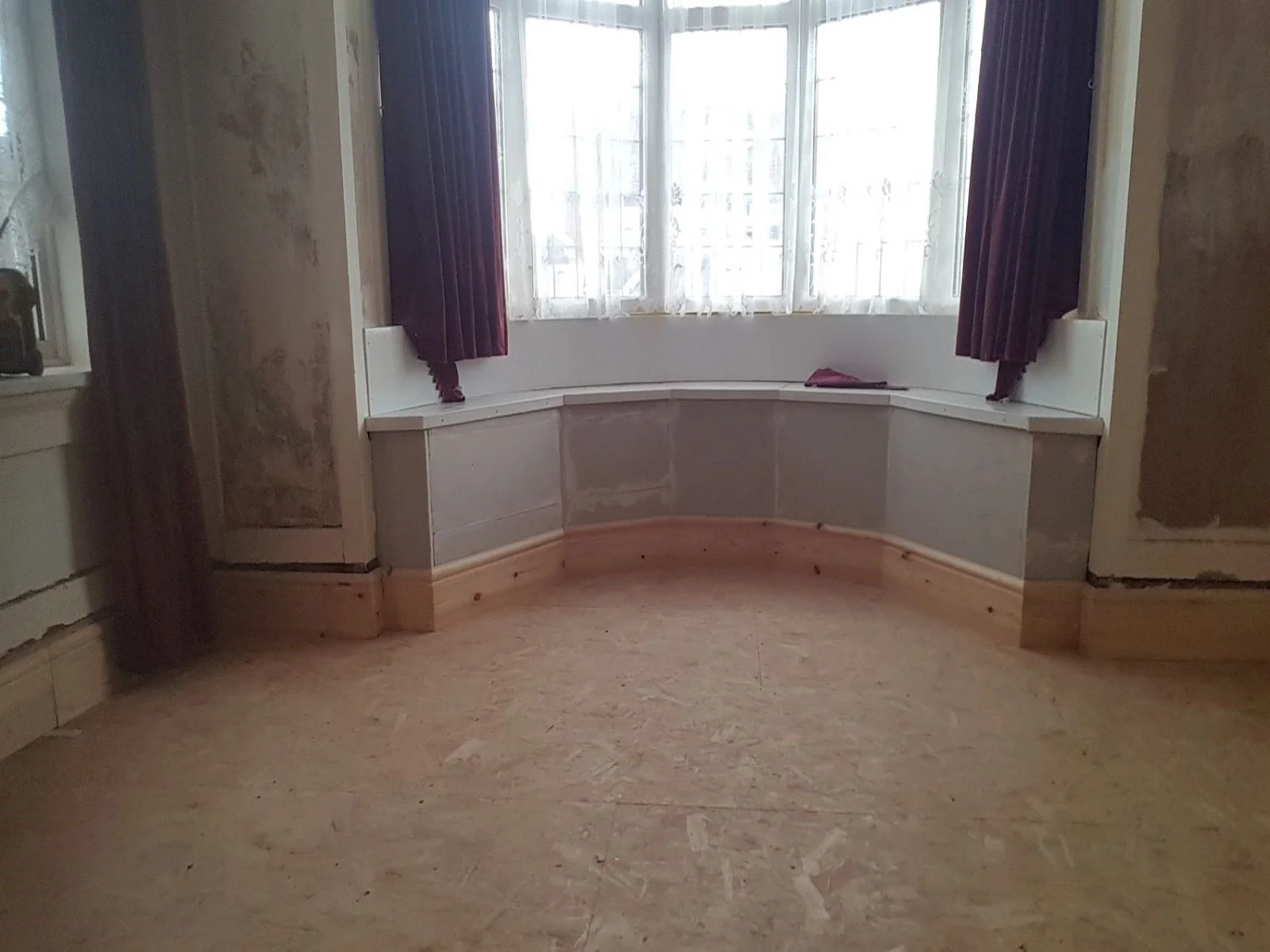 A sitting room under going a renovation, insulated and plasterboarded bay window, with new flooring and skirting boards