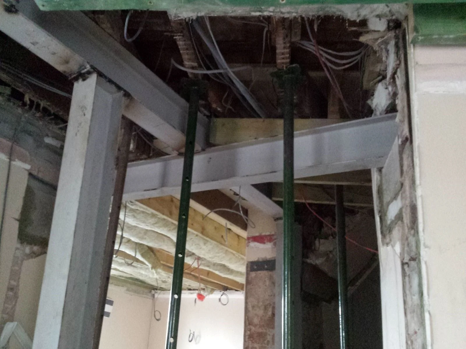 Structural home renovation featuring installed steel RSJ beams and adjustable metal acrow props supporting a temporary exposed ceiling structure.