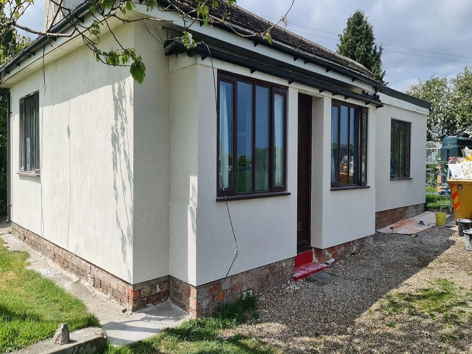 Detached bungalow exterior featuring newly applied off-white modern silicone render on the walls and dark wood window frames.
