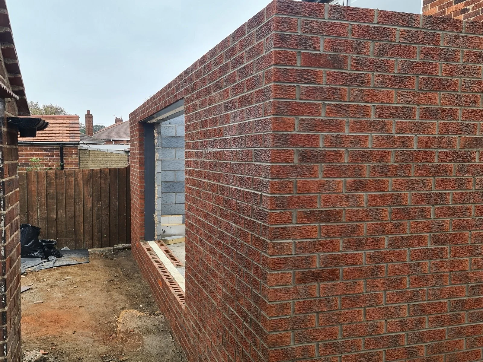 Modern single-storey brick home extension under construction, showing newly laid red facing brickwork with a large opening for bi-fold doors.