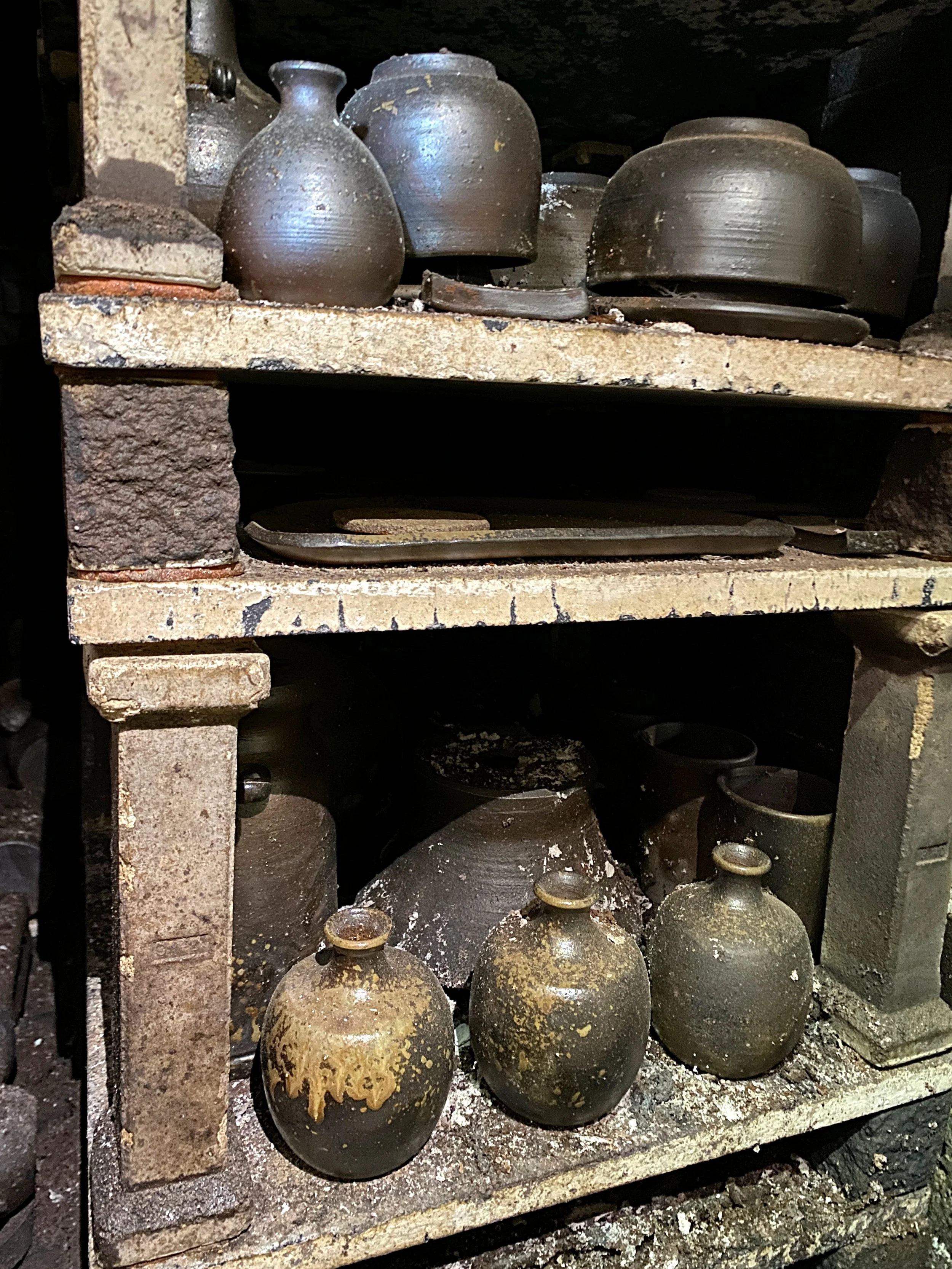 Post-firing kiln shelves showing ash-covered pieces and natural ash glaze.