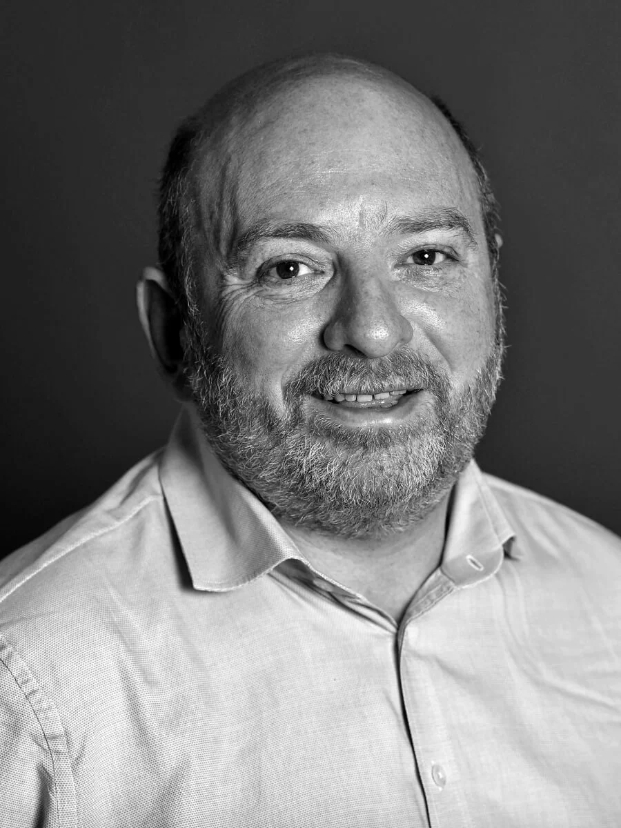 Black and white portrait of a man with a beard and mustache, wearing a collared shirt, smiling slightly, against a plain background.