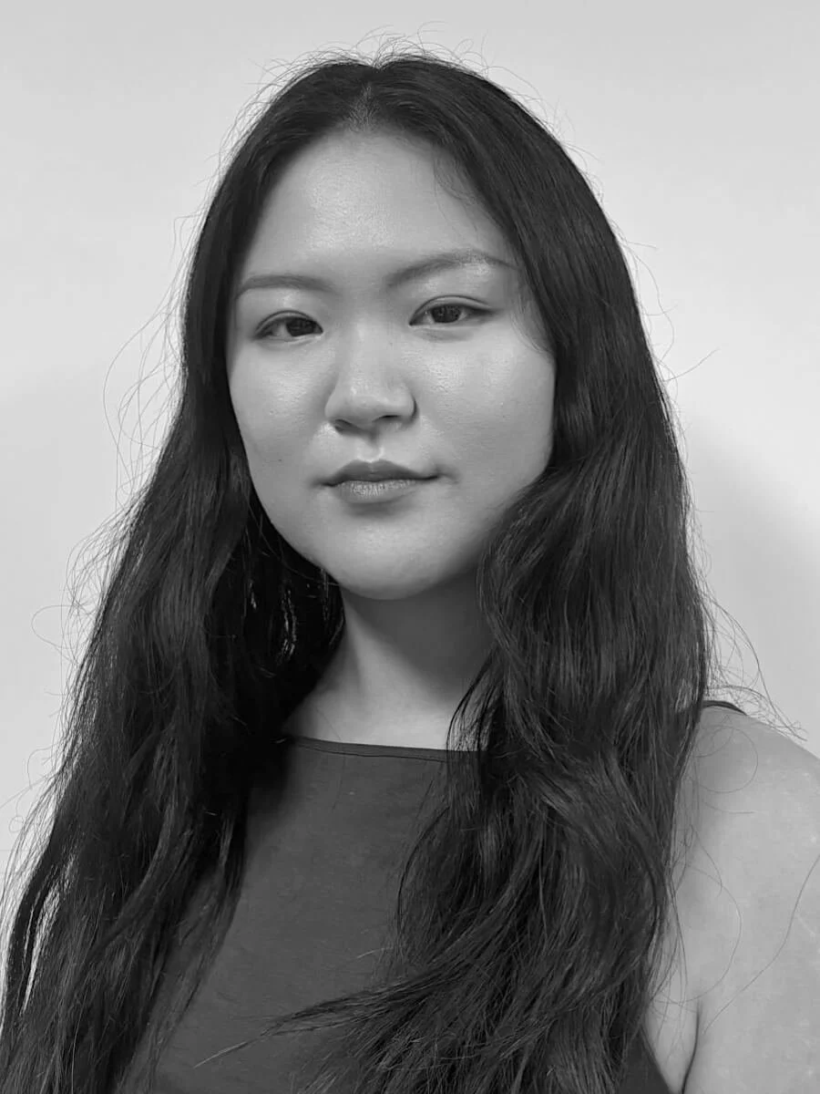 Black and white portrait of a woman with long wavy hair, wearing a sleeveless top, facing the camera with a neutral expression.
