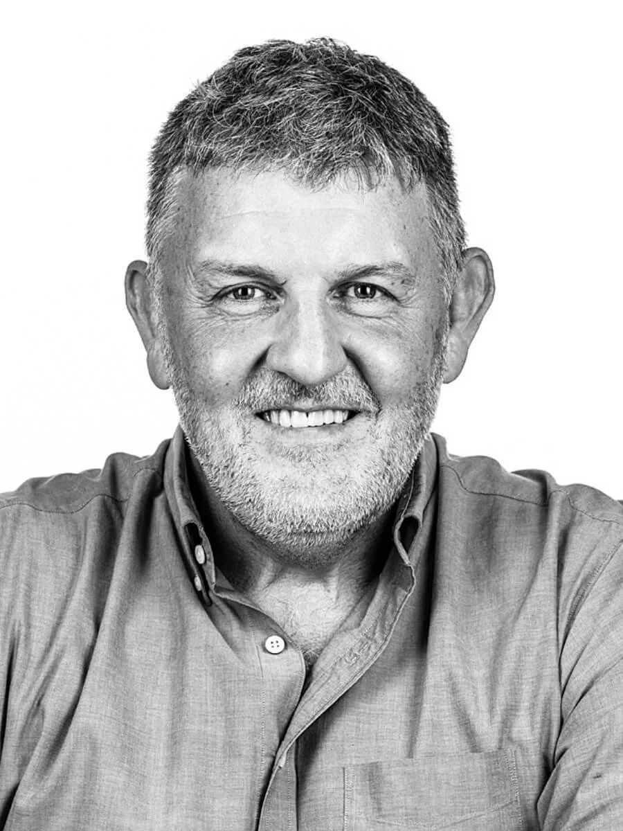 A black and white portrait of a smiling middle-aged man with short, graying hair and a beard, wearing a button-up shirt.