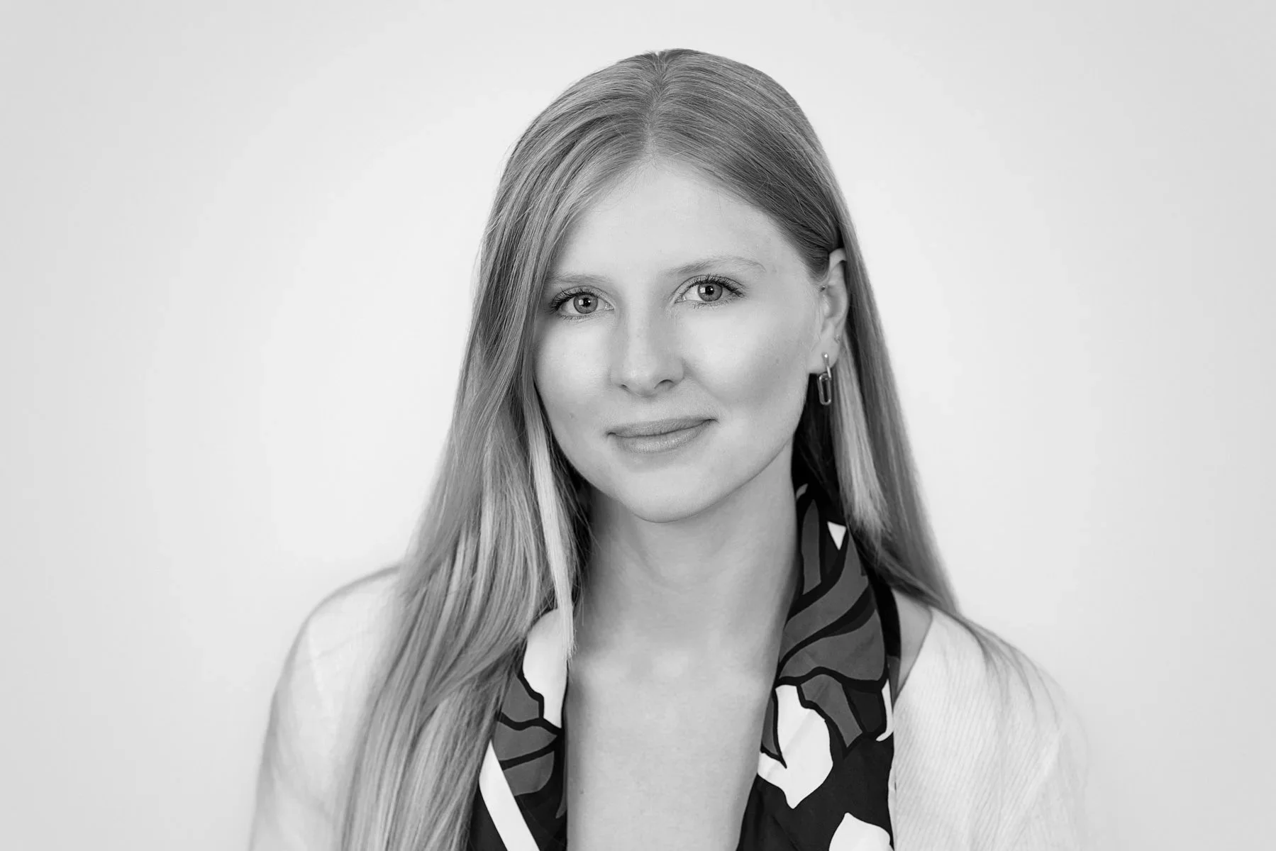 Black and white portrait of a woman with long hair, wearing earrings and a patterned scarf, smiling slightly, against a plain background.