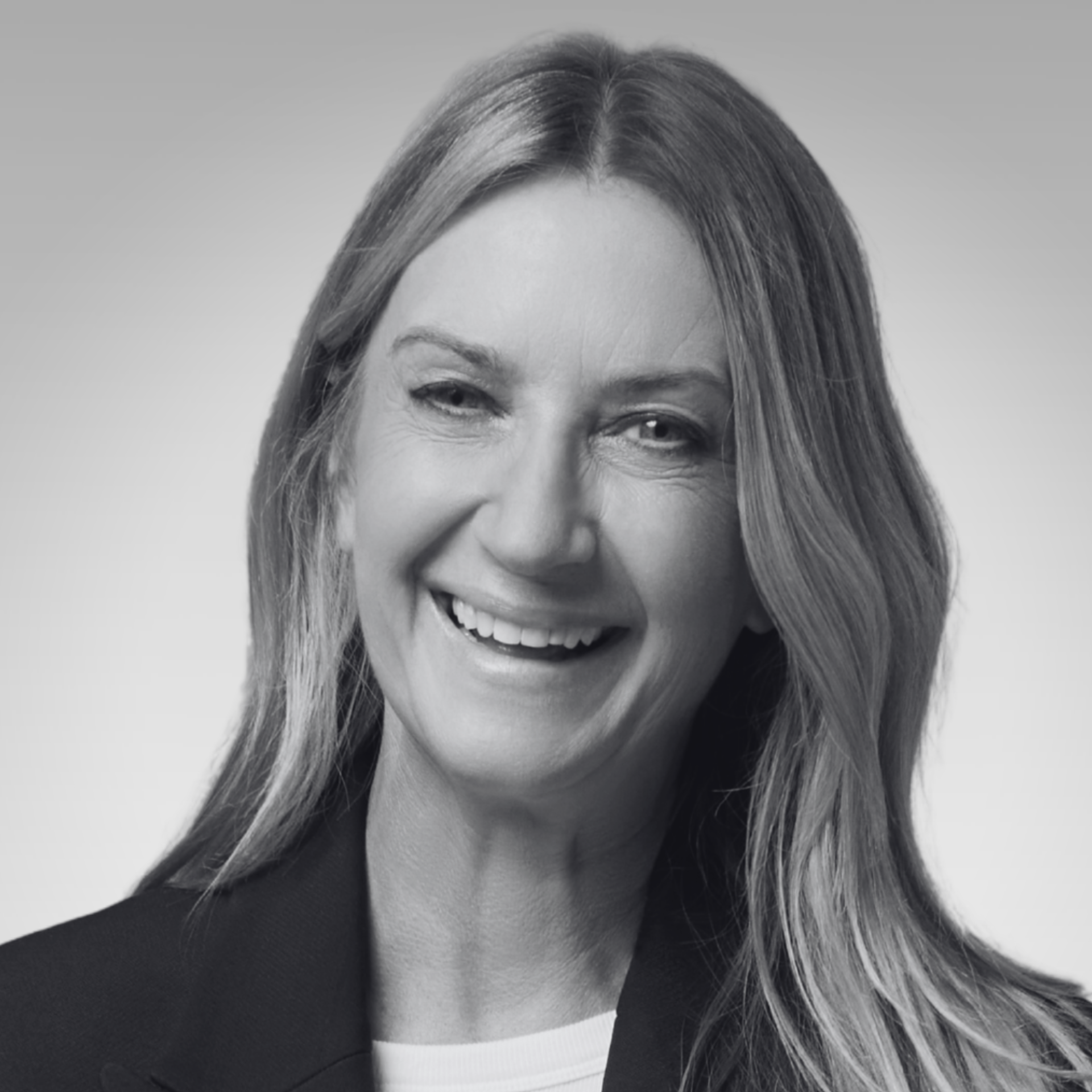 Black and white close-up photograph of a woman smiling and winking, with long straight hair, wearing a dark top and a light-colored undershirt.