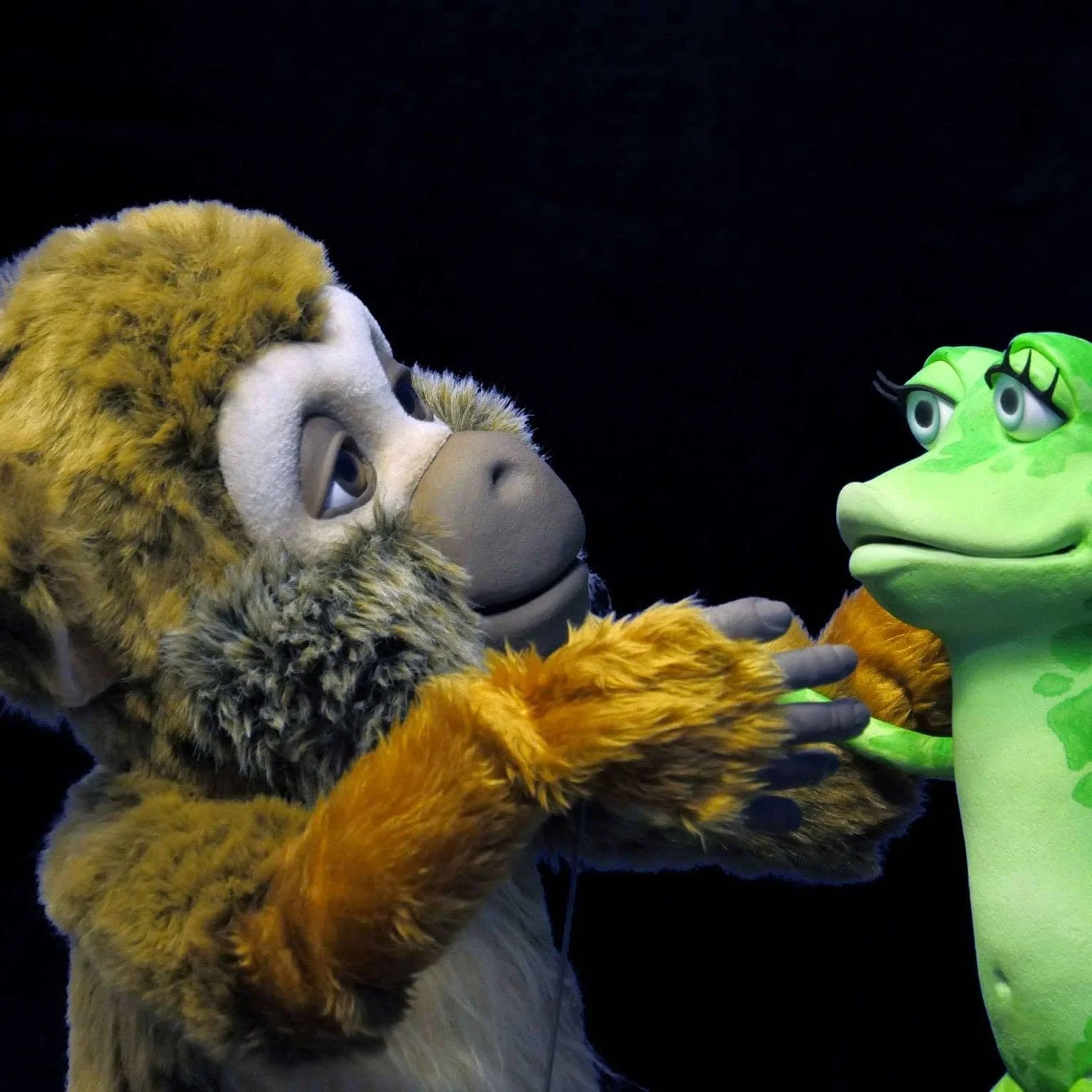 Une scène avec un lion en costume de peluche et une créature verte en plastique, semblable à un crocodile ou un alligator, se regardant.