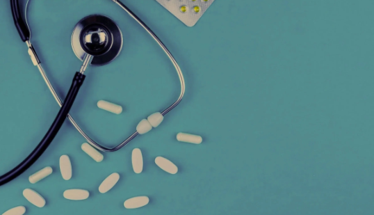 Medical stethoscope, white pills, and a blister pack of pills on a teal background.