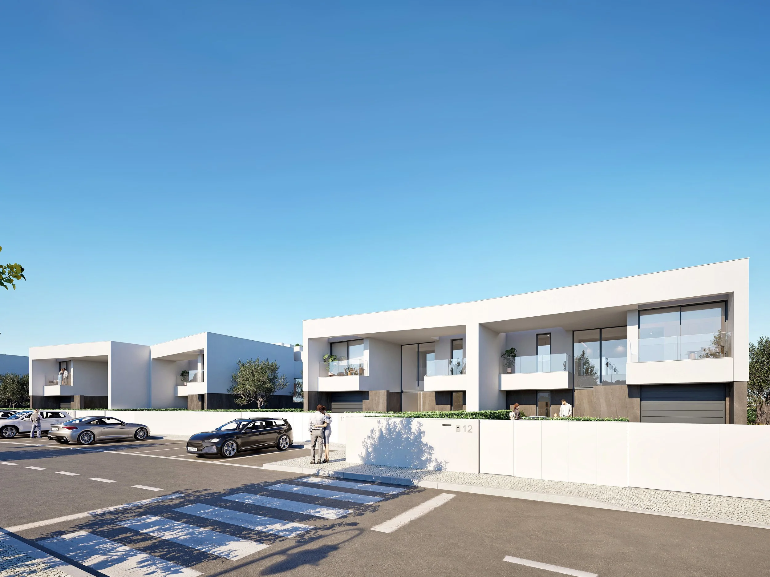 Modern white residential buildings with large glass windows and balconies, green bushes, parked cars, and people walking near the property beneath a clear blue sky.