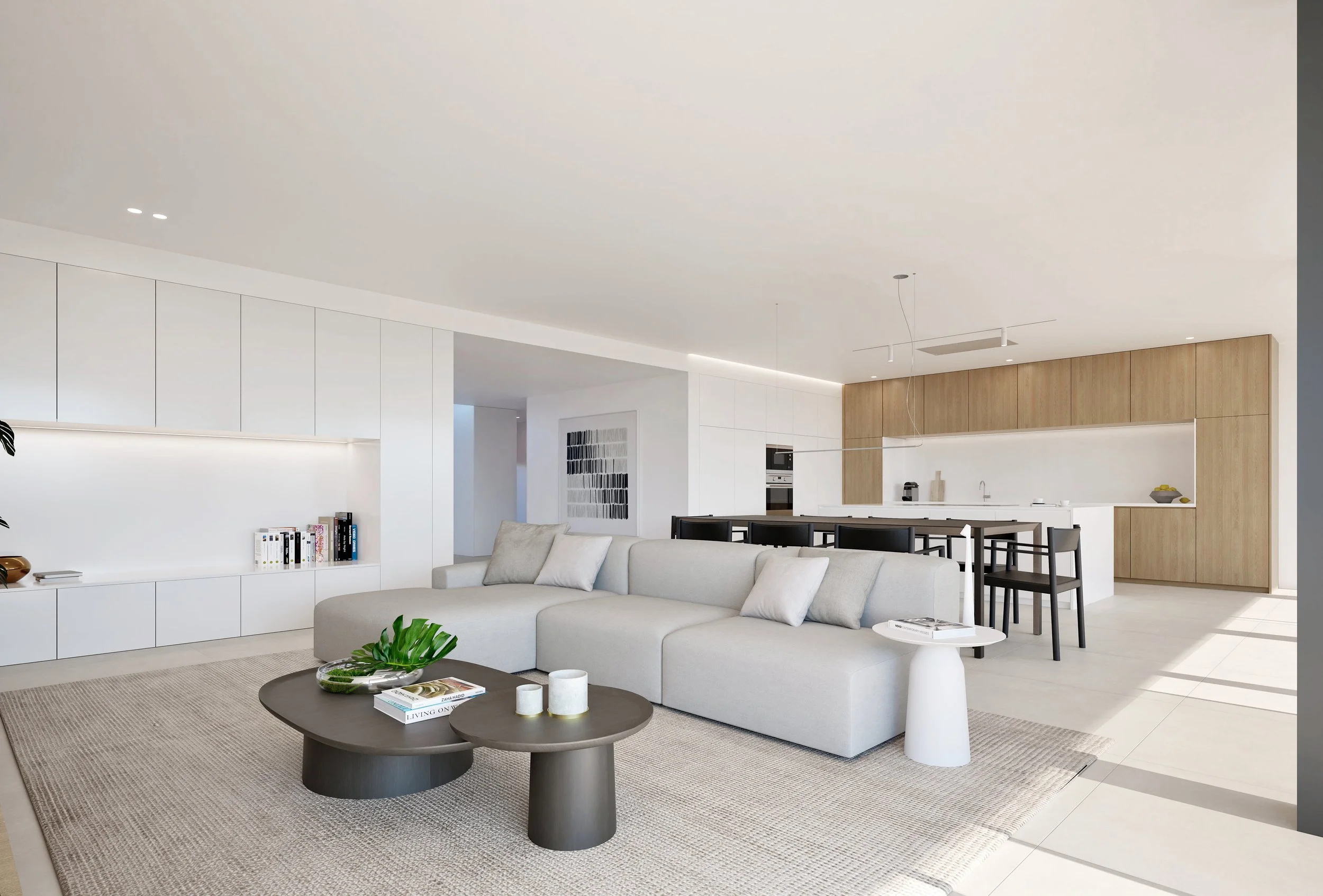 Modern open-concept living room and kitchen with white walls, beige sofa, two black nested coffee tables with books and candles, kitchenette with wooden cabinets, a white countertop, and black dining chairs.