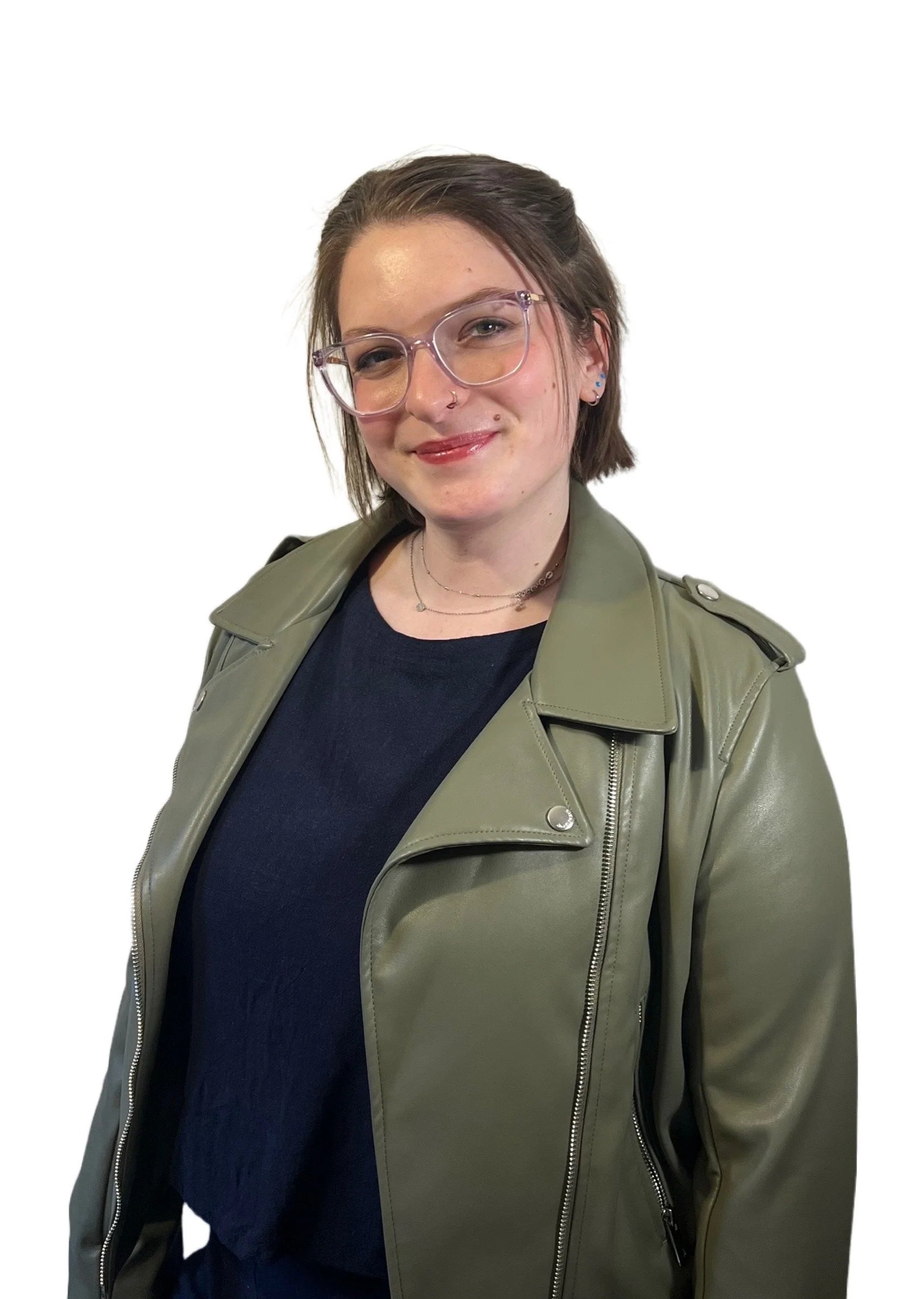 A woman with short brown hair, wearing large clear glasses, a nose ring, and small earrings, smiling and dressed in a black top and a green jacket against a plain white background.