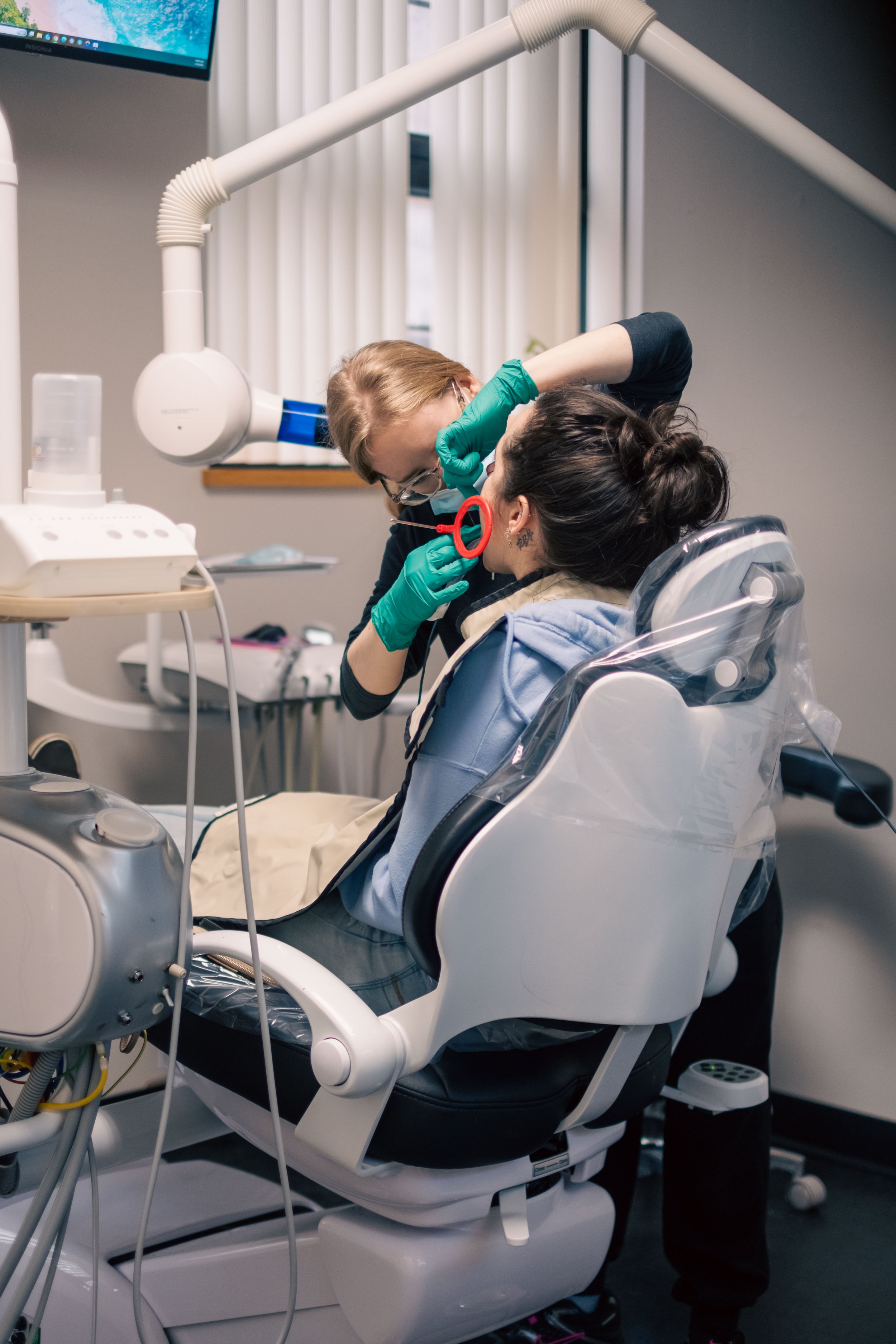 Dentist examining a patient in a dental chair with dental equipment and a monitor in the background.