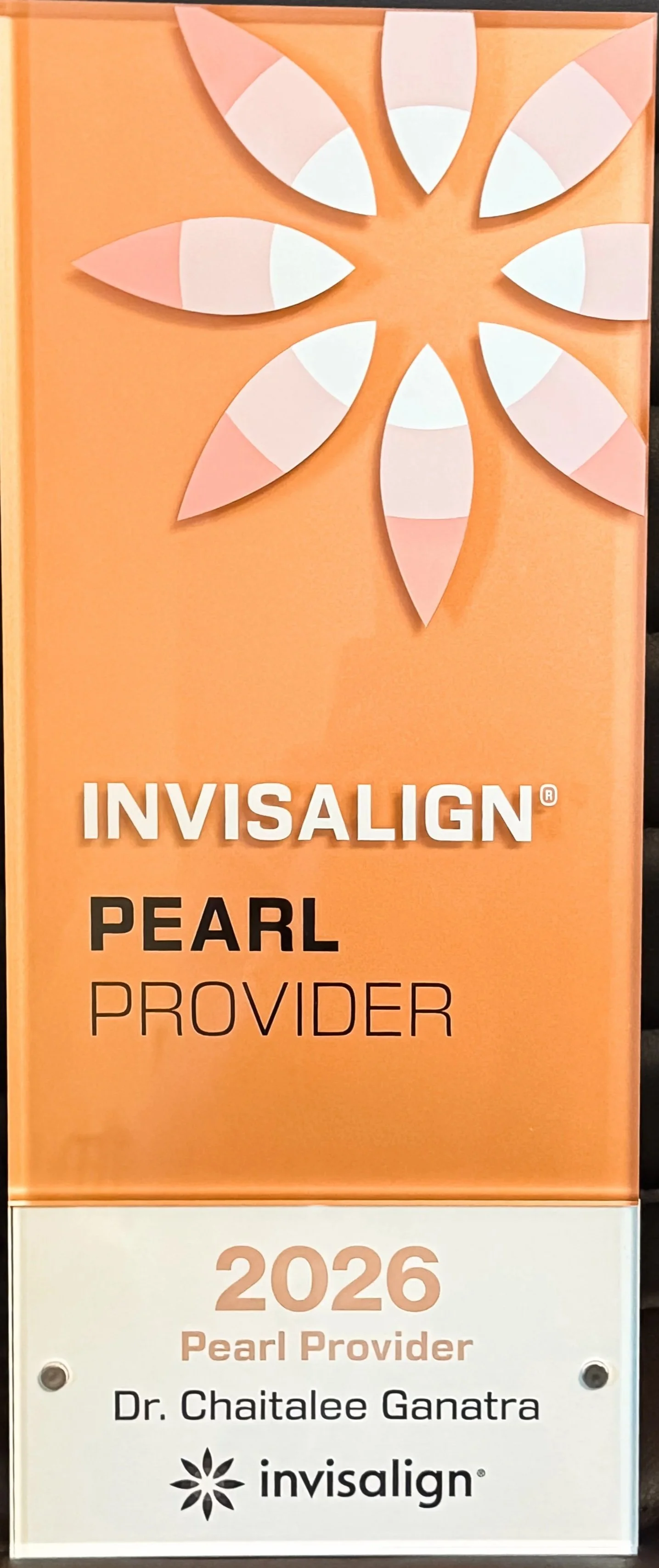 Sign celebrating Dr. Chaitalee Ganatra as the 2026 Invisalign Pearl Provider with a pink and white design featuring a flower-like pattern.