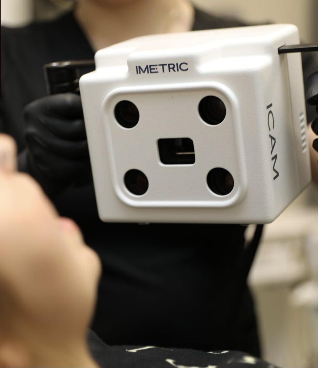 Close-up of an IMACTIC industrial inspection device with four lenses and a central sensor, held by a person in black gloves.