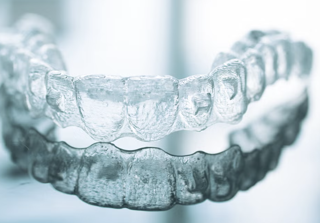 Close-up of a clear dental or orthodontic aligner with reflections, resting on a reflective surface under soft lighting.