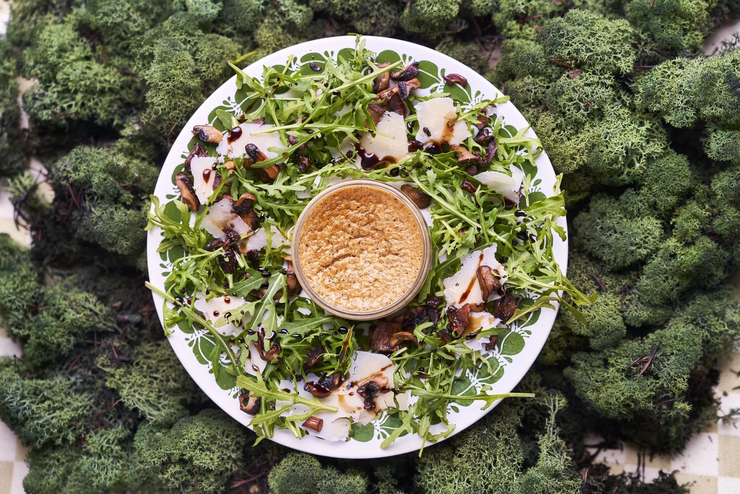 Een paddenstoelen custard met een groene salade, geraspte kaas, noten en een dressing, op een groene, mosachtige achtergrond.