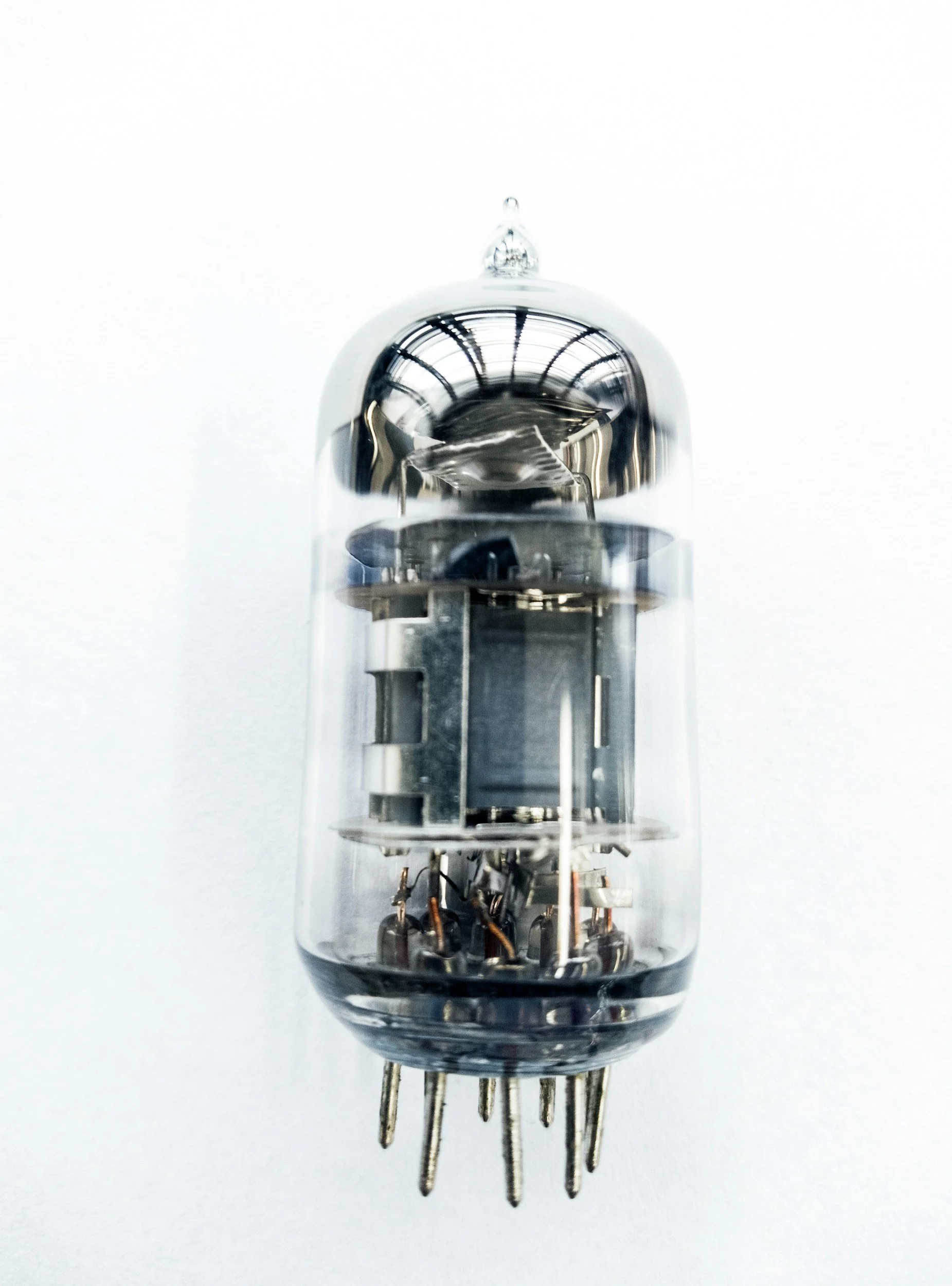 Close-up of a vacuum tube electronic component with metal pins at the bottom, glass enclosure, and internal wiring visible, set against a white background.