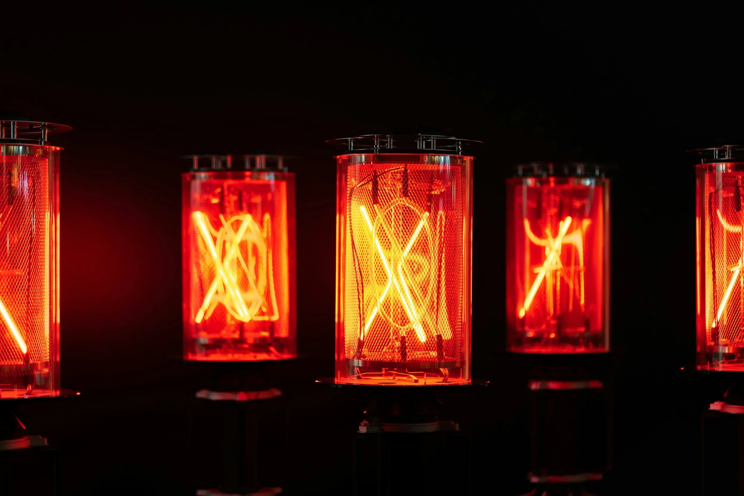 Five glowing red neon light bulbs against a black background, each with an intricate filament design inside