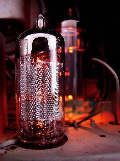 Close-up of a glass vacuum tube with internal components, glowing with orange light in a laboratory or electronic setup.