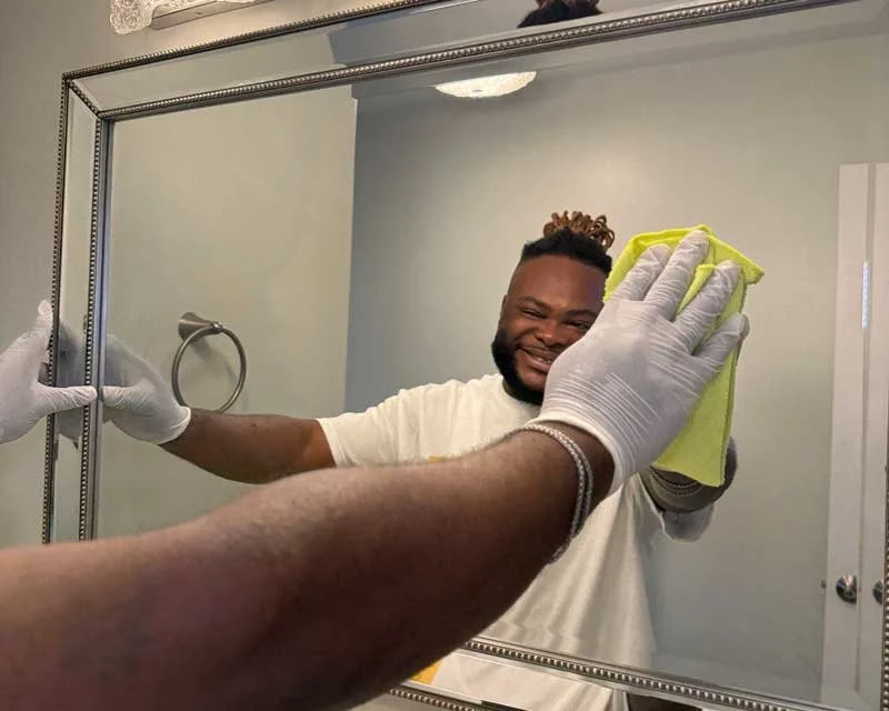 Smiling black man cleaning a mirror