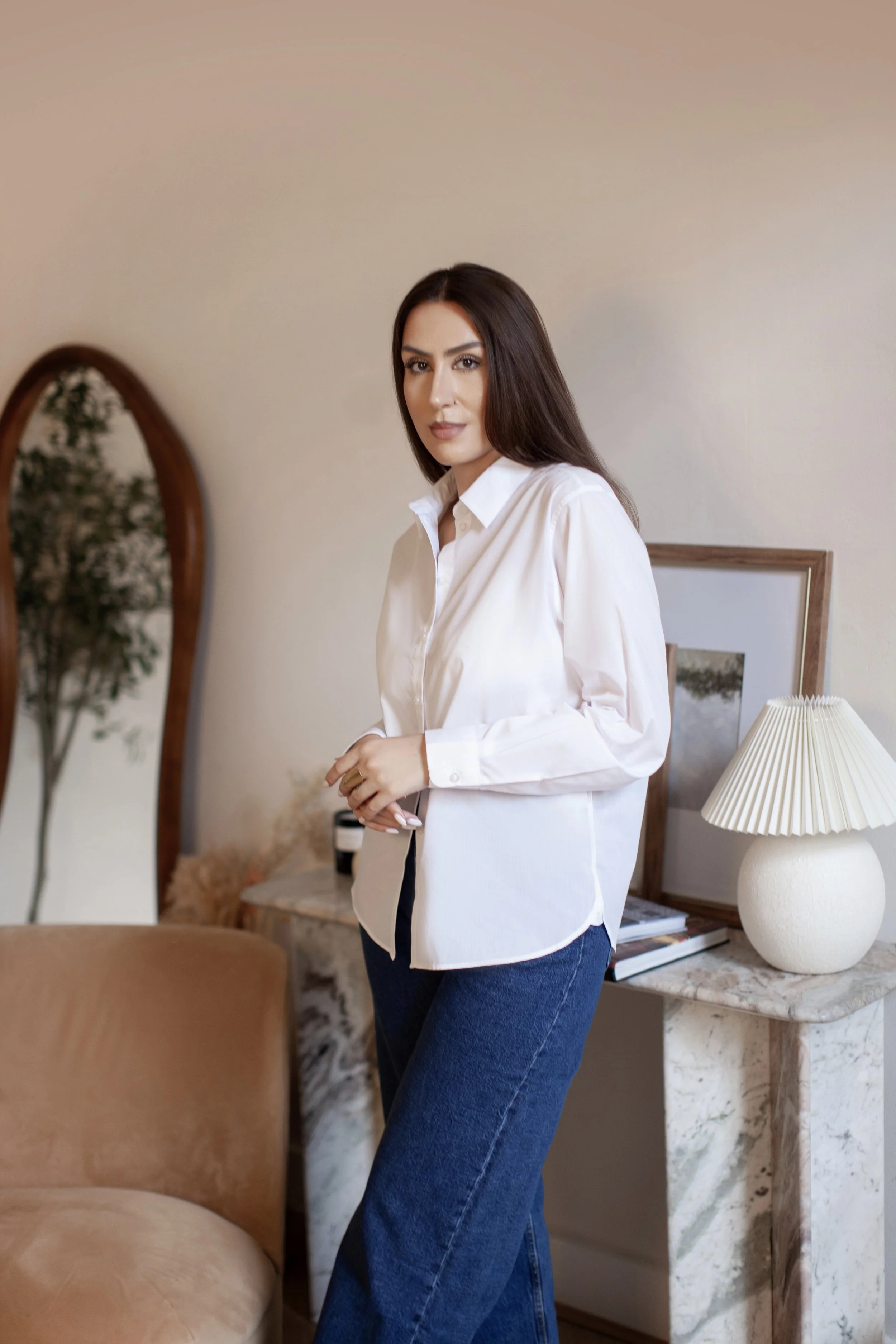 Oana Barabasa, feminine refinement mentor of Atelier Privé within Feminine Signature brand, standing in an elegant interior wearing a white shirt and blue jeans.