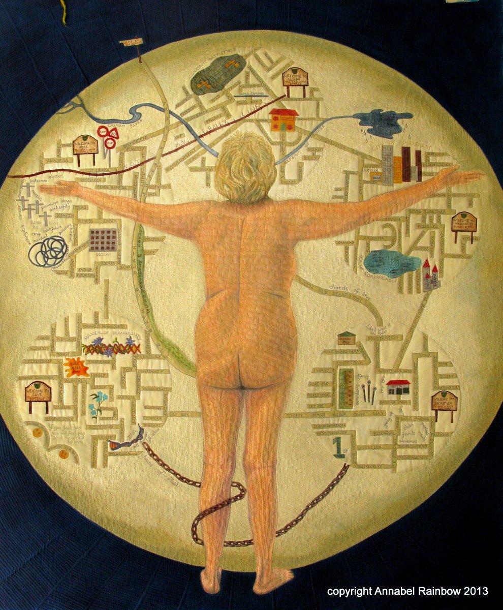 An art quilt by Annabel Rainbow showing a Life Story. A figure standing with arms outstretched, set against a map-like background with various symbols and patterns. The scene is circular and surrounded by a darker border.