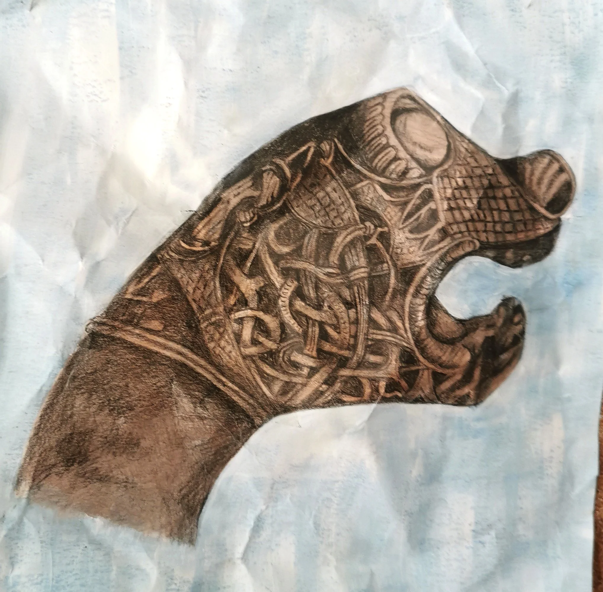 Artistic drawing of an intricately patterned animal head, resembling a dragon with Celtic designs on blue background.