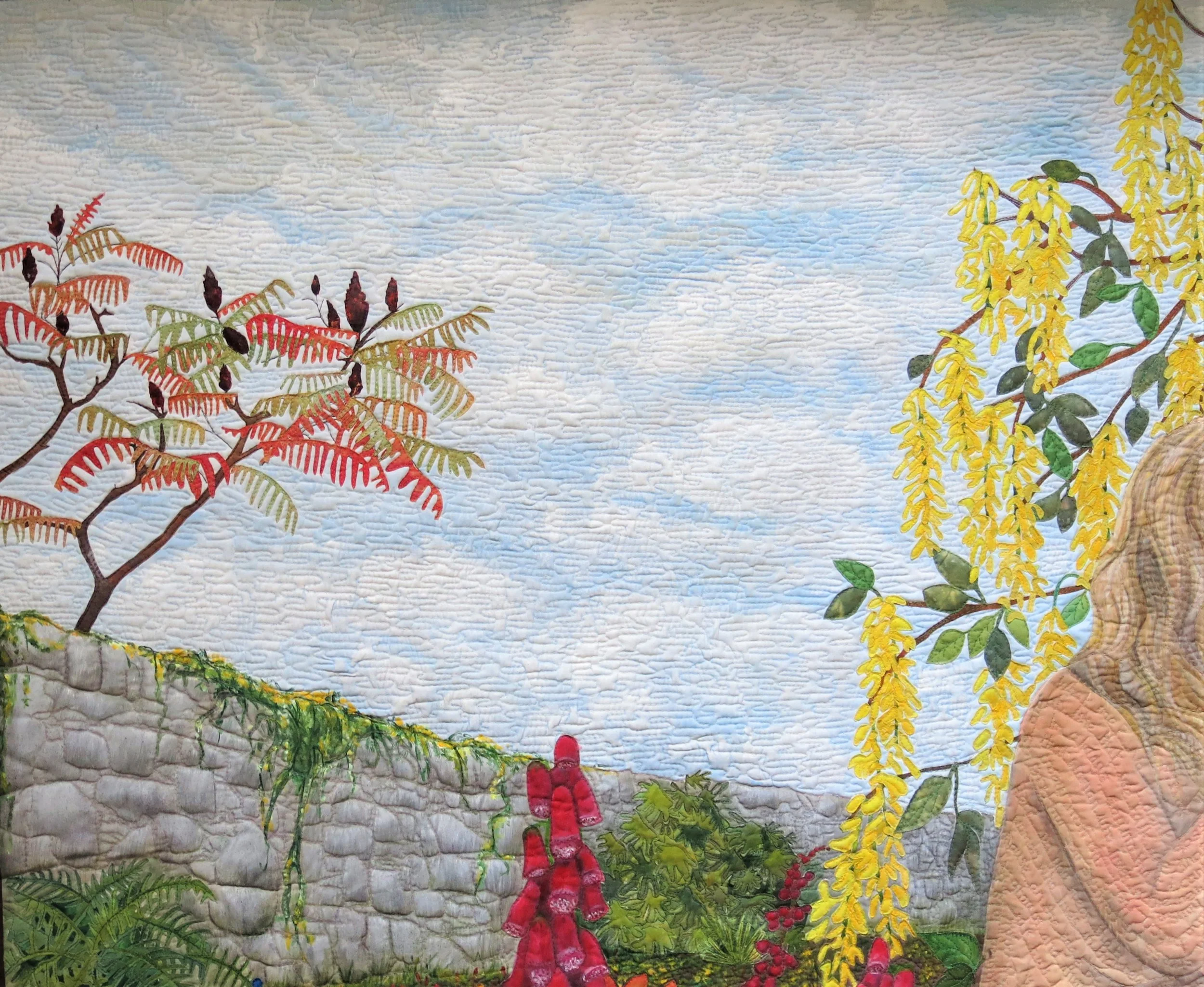A quilt with a landscape scene featuring trees, yellow hanging flowers, green foliage, and a stone wall with a blue sky background.