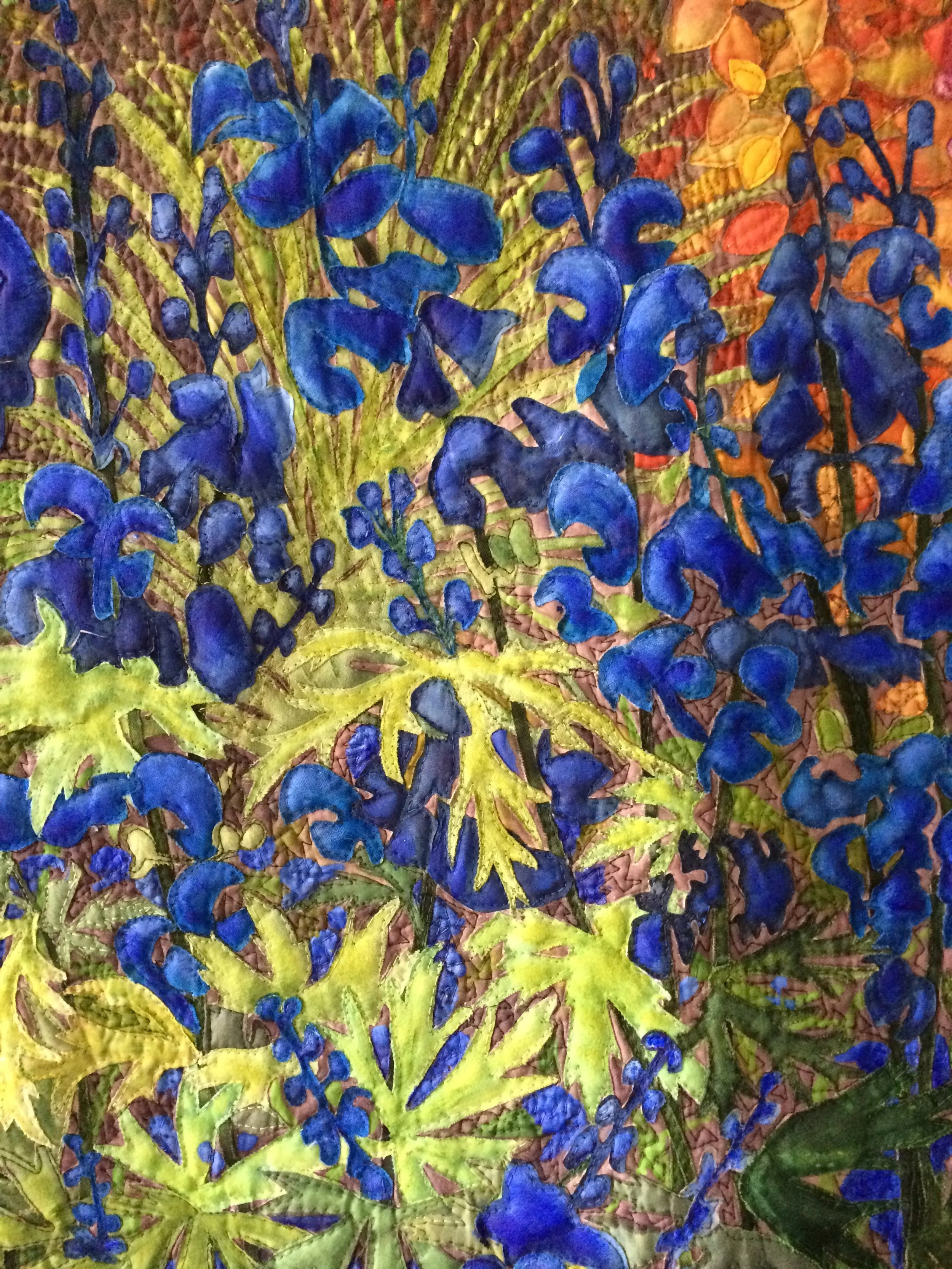 Abstract quilt art featuring blue flowers and green leaves on a multicolored background.