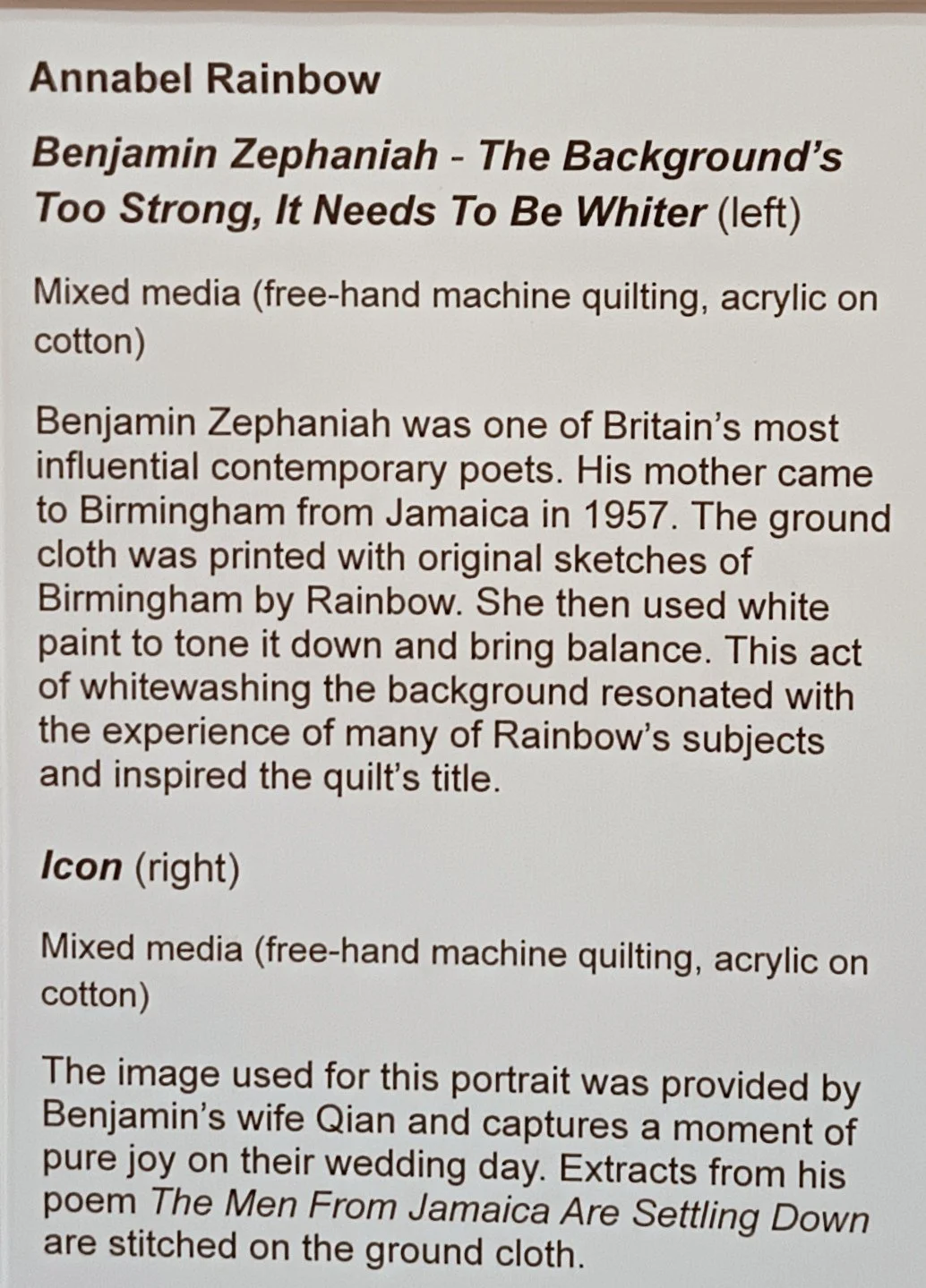 Exhibit label describing two mixed media artworks by Annabel Rainbow. The first piece, titled "Benjamin Zephaniah - The Background's Too Strong, It Needs To Be Whiter," features free-hand machine quilting with acrylic on cotton, inspired by the poet Benjamin Zephaniah and his mother's sketches of Birmingham. The second piece, titled "Icon," captures a joyful moment of Benjamin's wife Qian on their wedding day, with extracts from his poem "The Men From Jamaica Are Settling Down" stitched on the ground cloth.