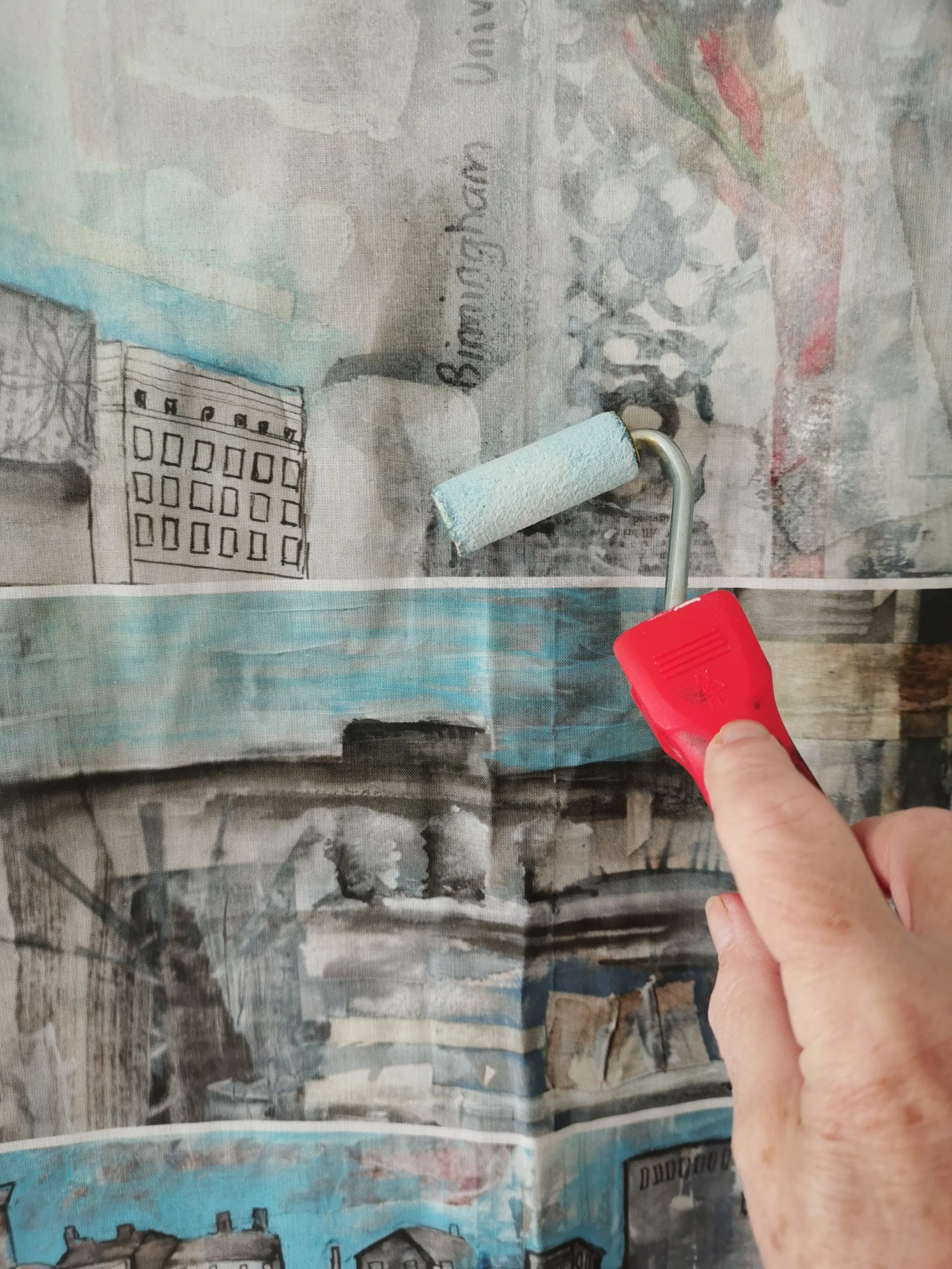 Hand using a red-paint roller on abstract artwork with buildings and text "Birmingham" visible.