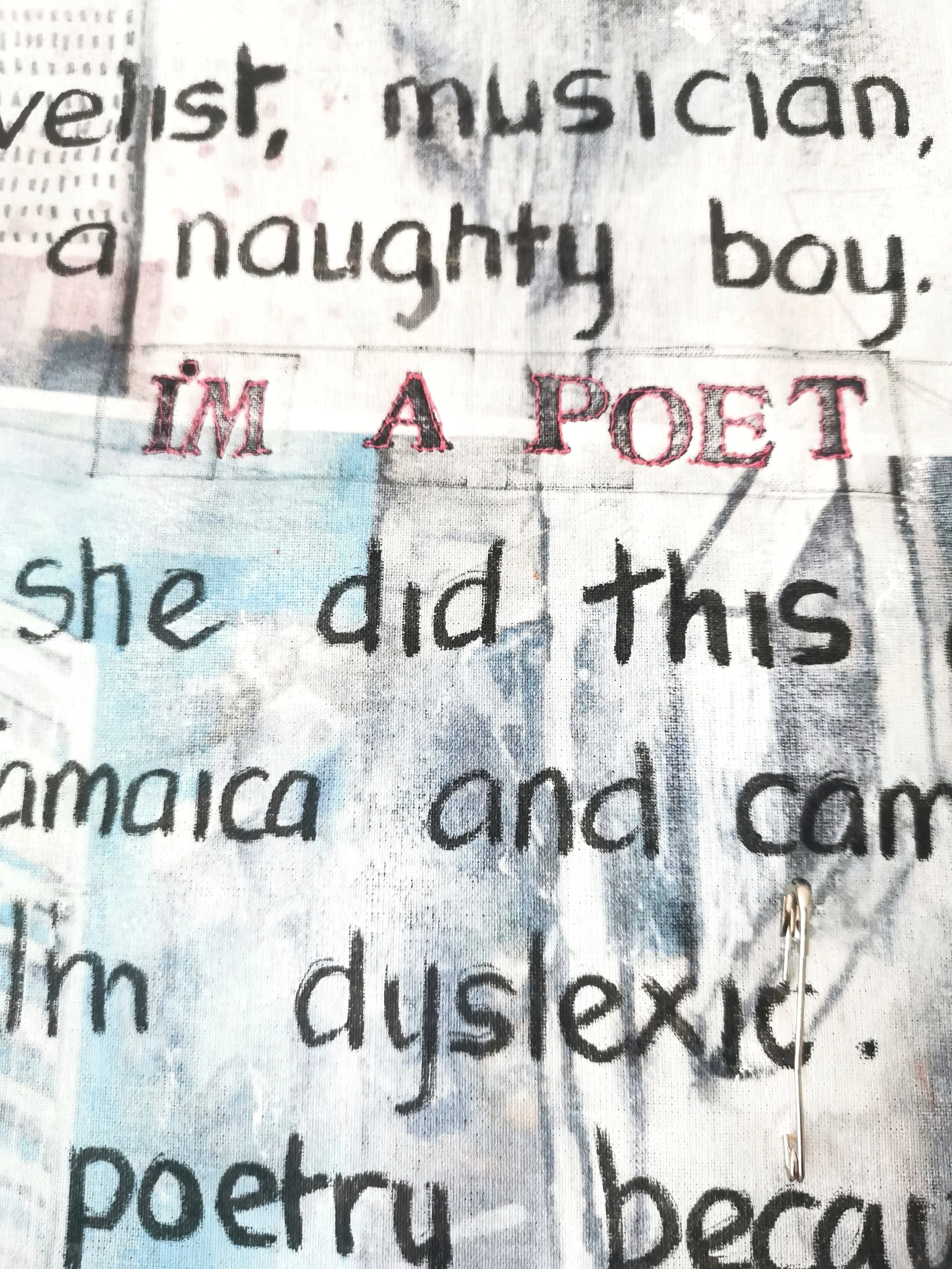Text on fabric with the phrases "I'm a poet" stitched in red and various sentences printed in black, including words about being a musician, a naughty boy, dyslexic, Jamaica, and more. A safety pin is attached.